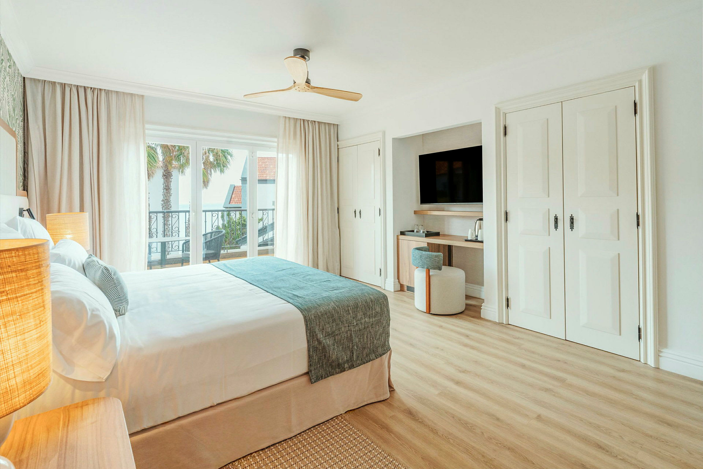 Et lyst, moderne hotelværelse med en dobbeltseng, stort vindue, balkon og et velordnet skrivebord med tv. (AI-genereret tekst)