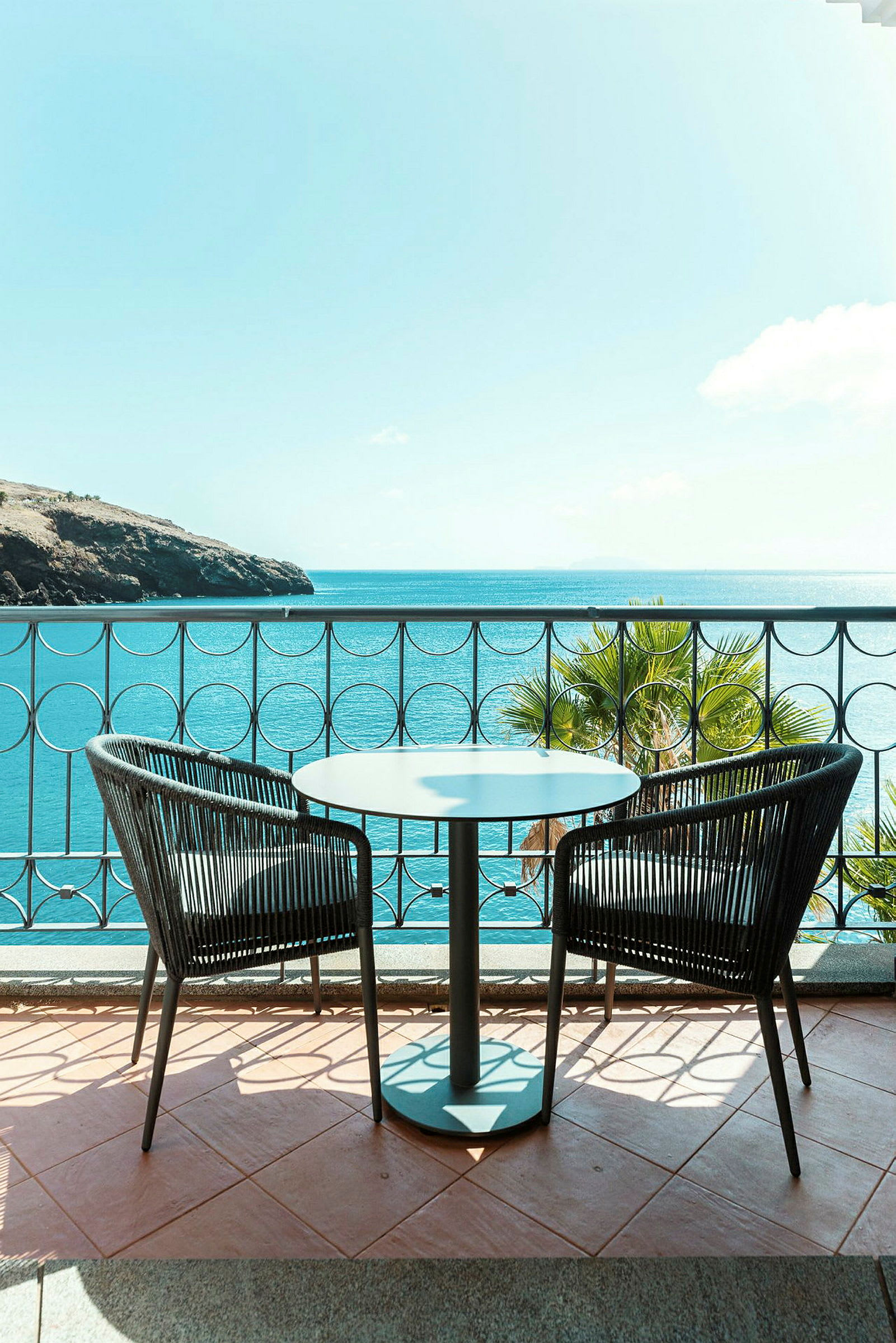 Et bord med to stole på en balkon med udsigt over havet. (AI-genereret tekst)