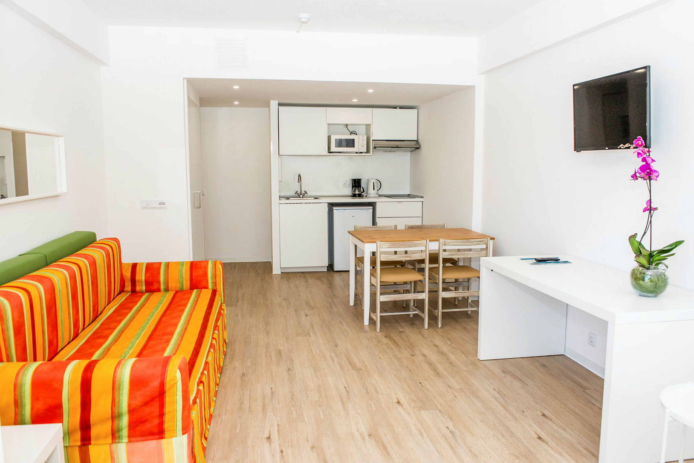 Billede af et moderne hotelværelse med sofa, spisebord, køkkenområde og TV. (AI-genereret tekst)
