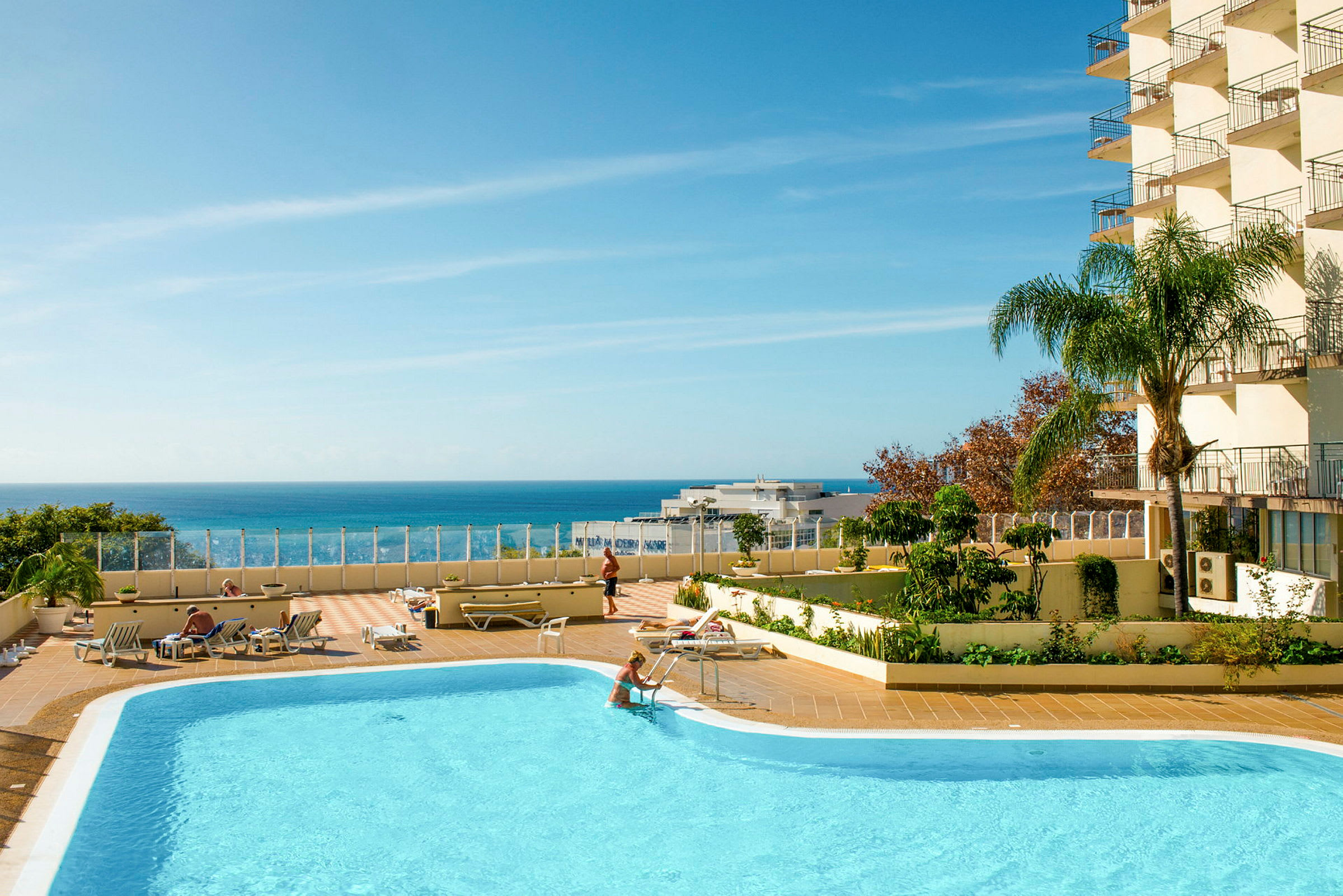 En udendørs swimmingpool med liggestole og en klar blå himmel over havet. (AI-genereret tekst)