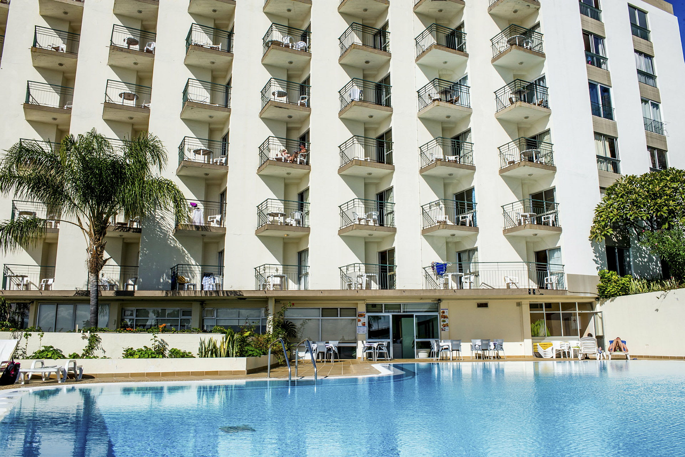 Hotellets facade med flere altaner over en swimmingpool. (AI-genereret tekst)