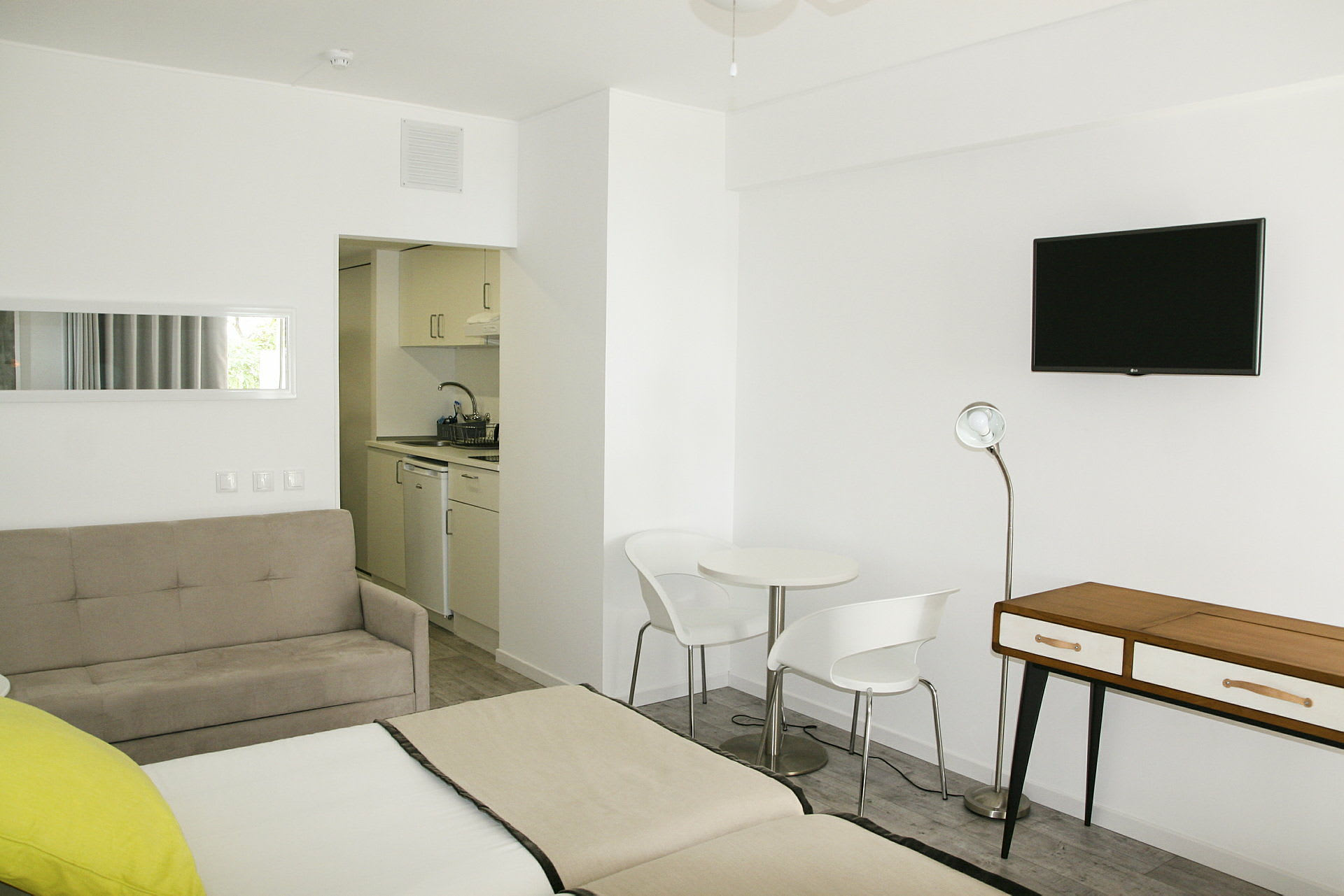 Et moderne hotelværelse med hvide vægge, en siddegruppe og et mindre køkken. (AI-genereret tekst)