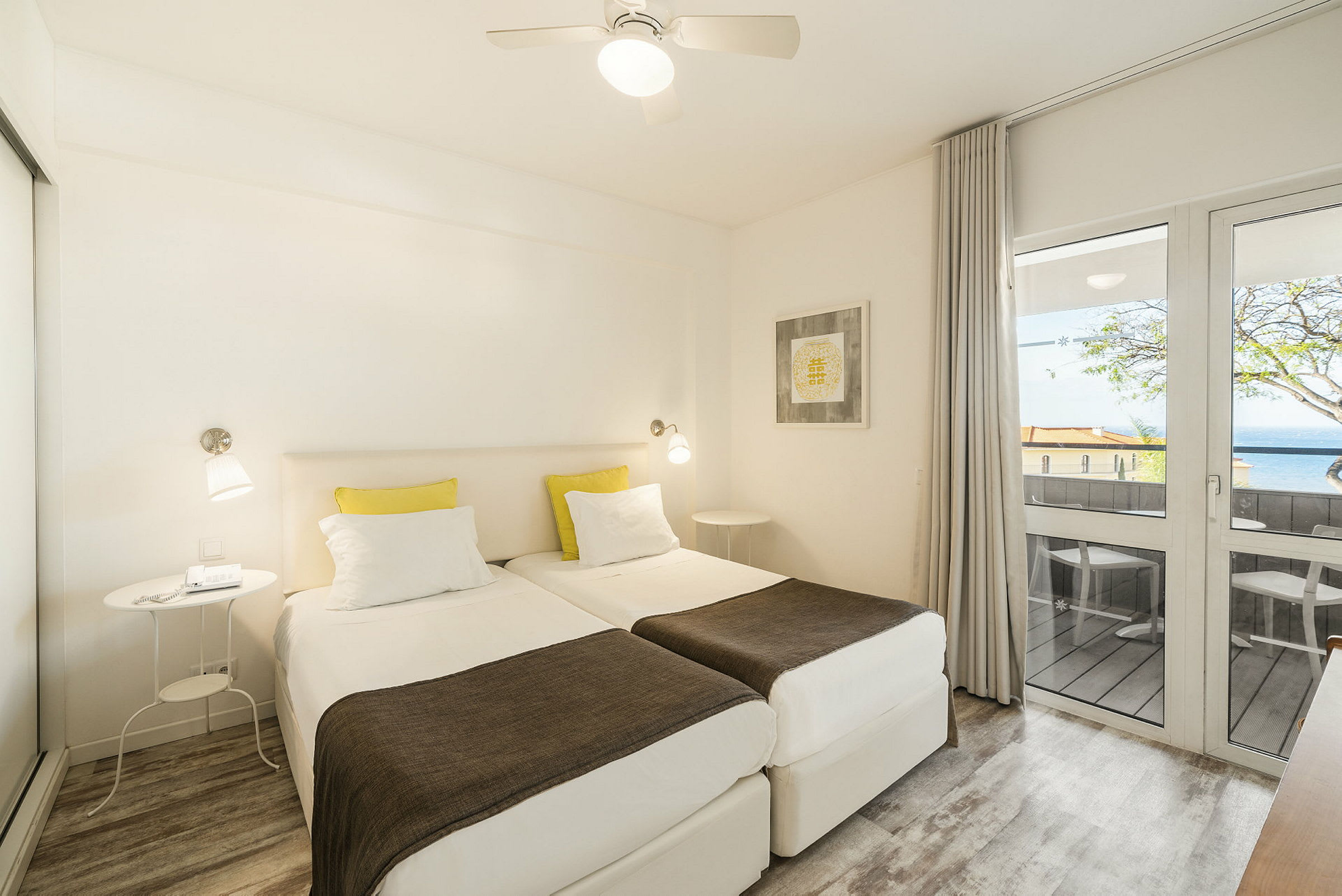 Et hotelværelse med to enkeltsenge, en balkon med udsigt og lyse møbler. (AI-genereret tekst)