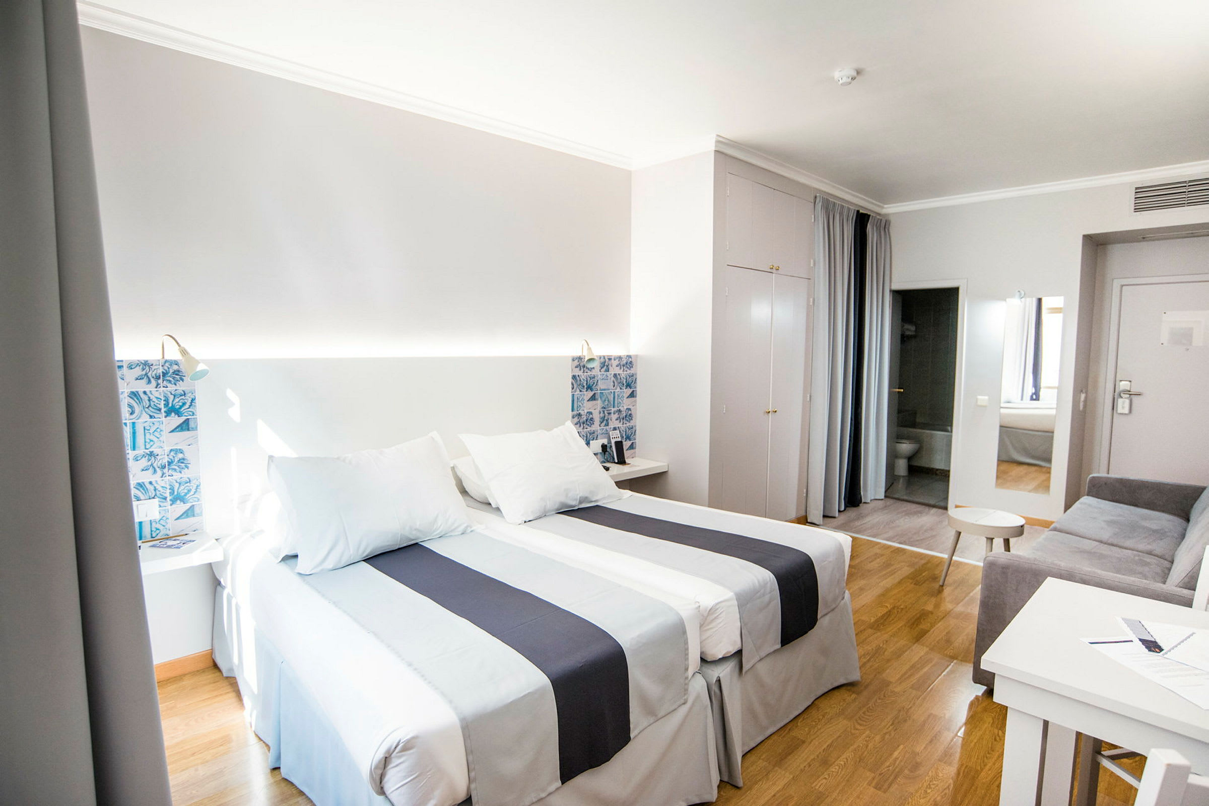 Hotelværelse med to enkeltsenge med hvidt og blåt sengetøj. (AI-genereret tekst)