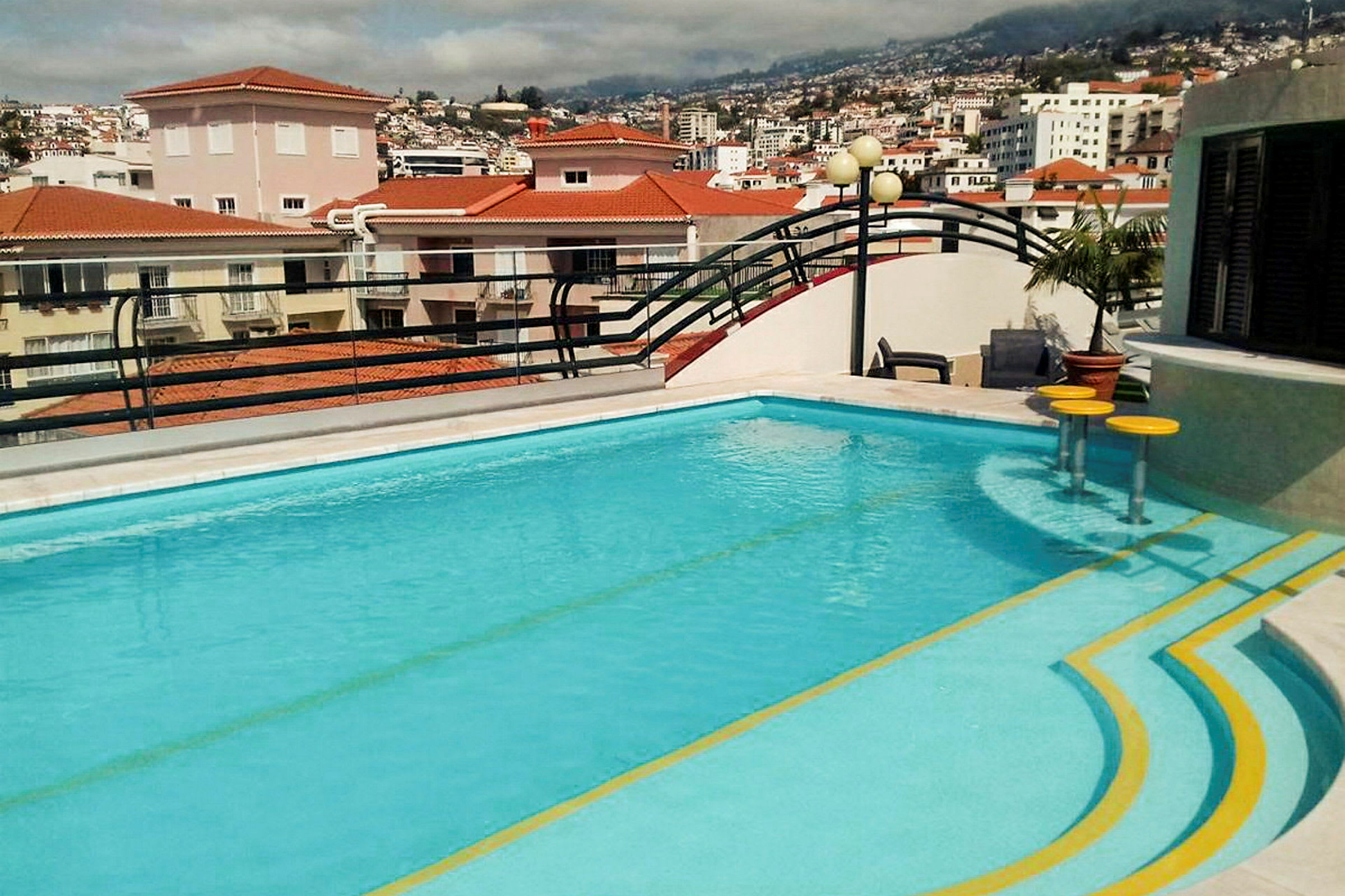 En udendørs swimmingpool på en terrasse med udsigt over tagene i en by. (AI-genereret tekst)