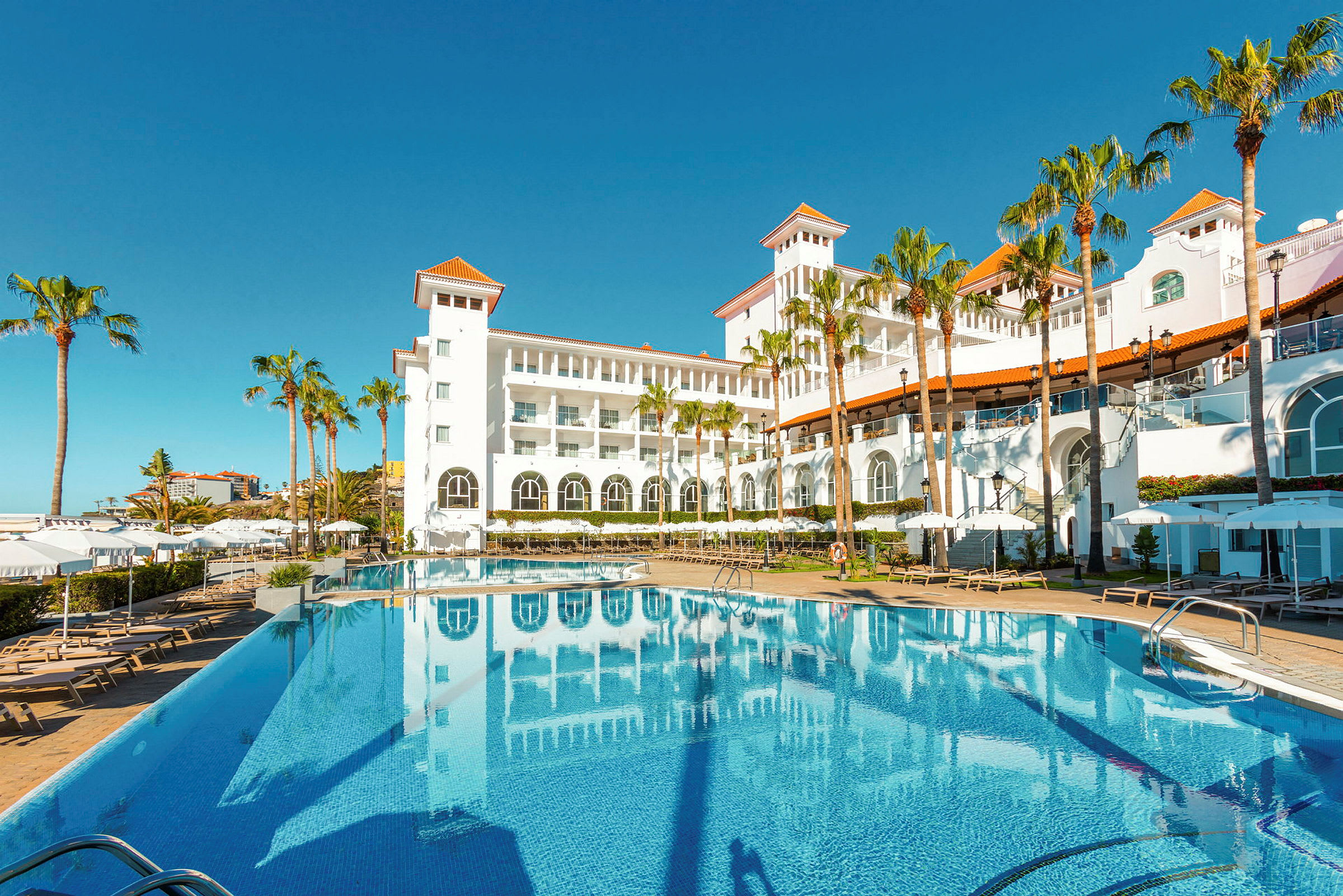 Hotel med hvid facade og pool i forgrunden. (AI-genereret tekst)