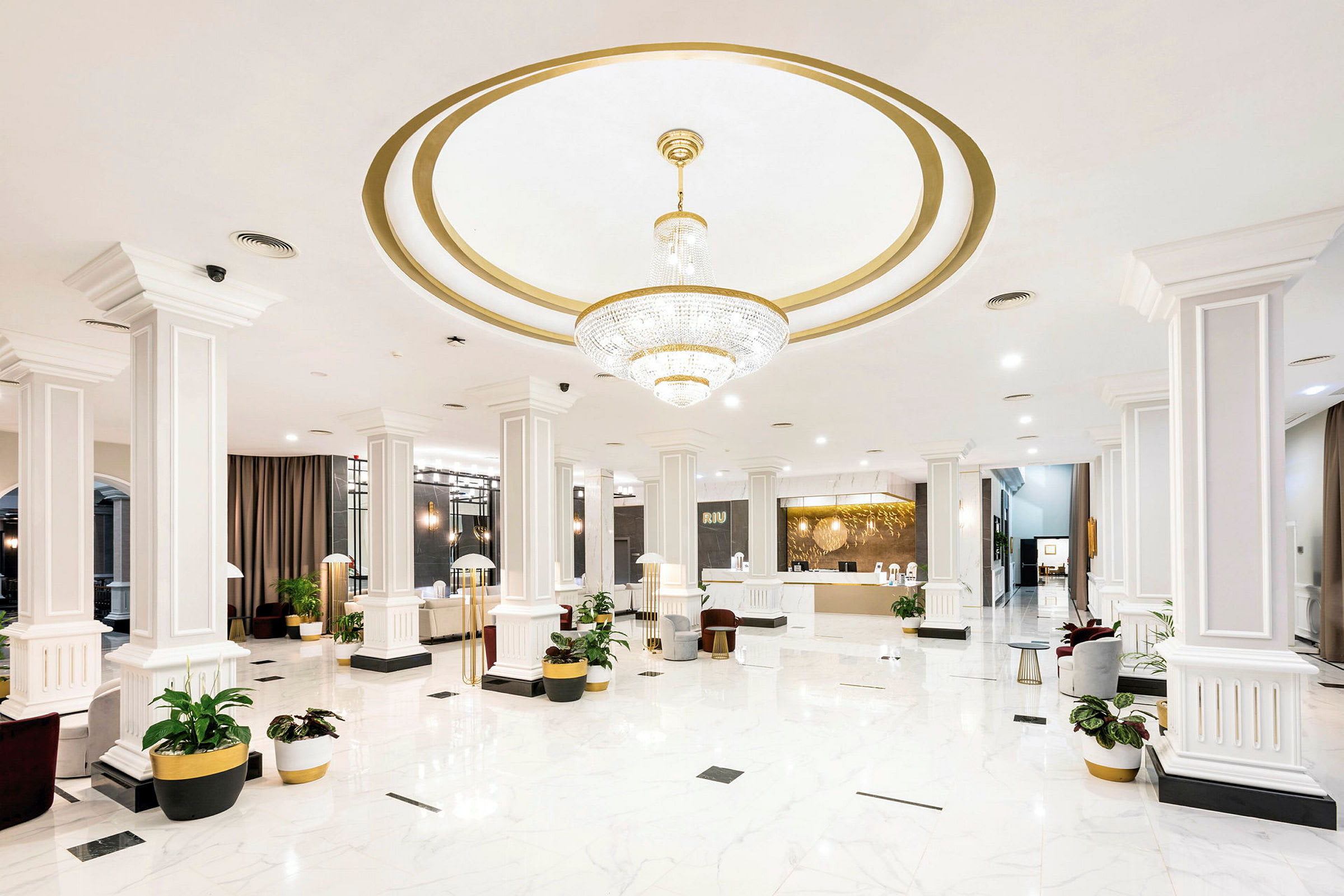 Hotellets lobby med hvid marmorgulv, søjler og en stor lysekrone. (AI-genereret tekst)