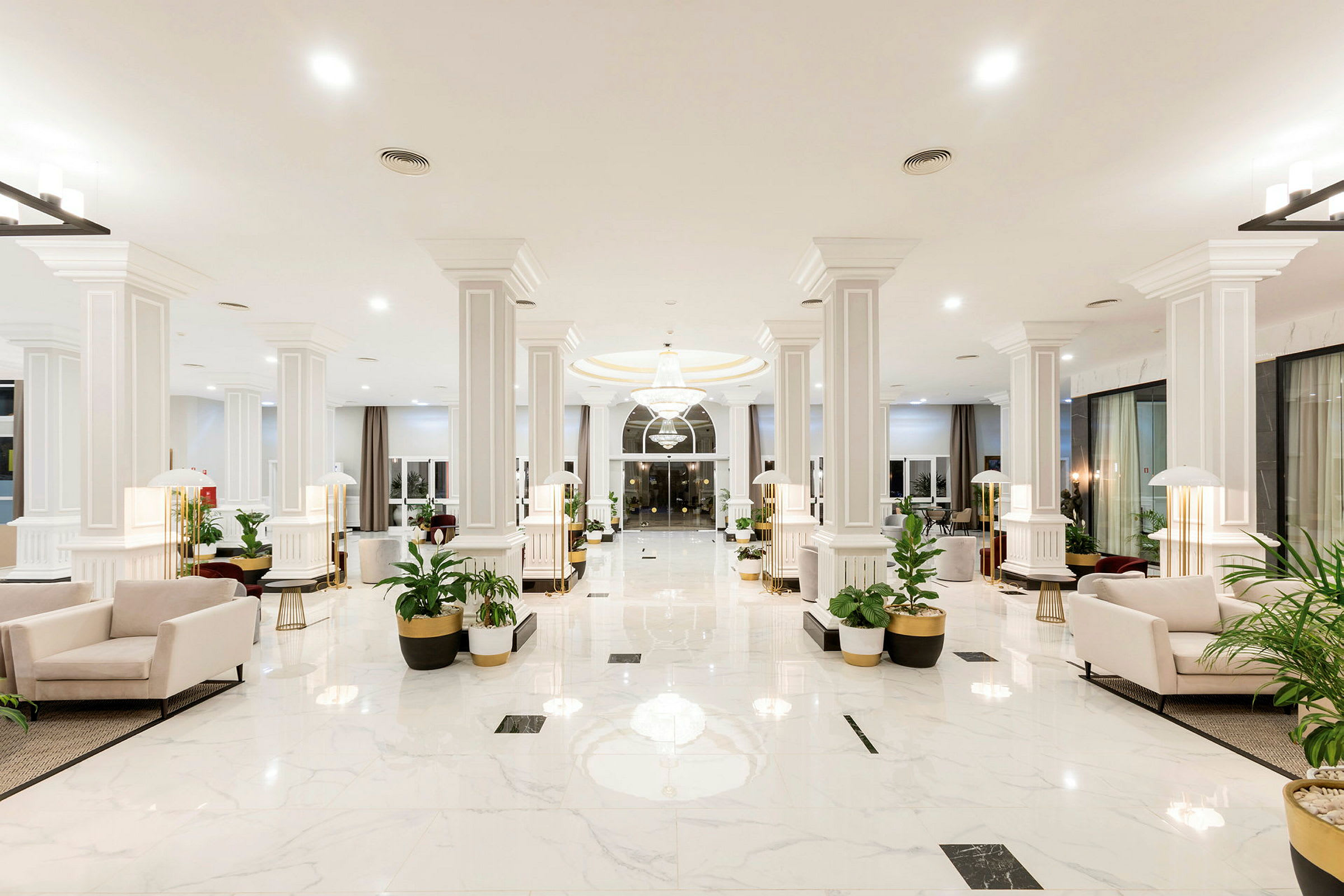Lys og rummelig hotellobby med hvide marmorgulve, lyse siddegrupper og grønne planter. (AI-genereret tekst)