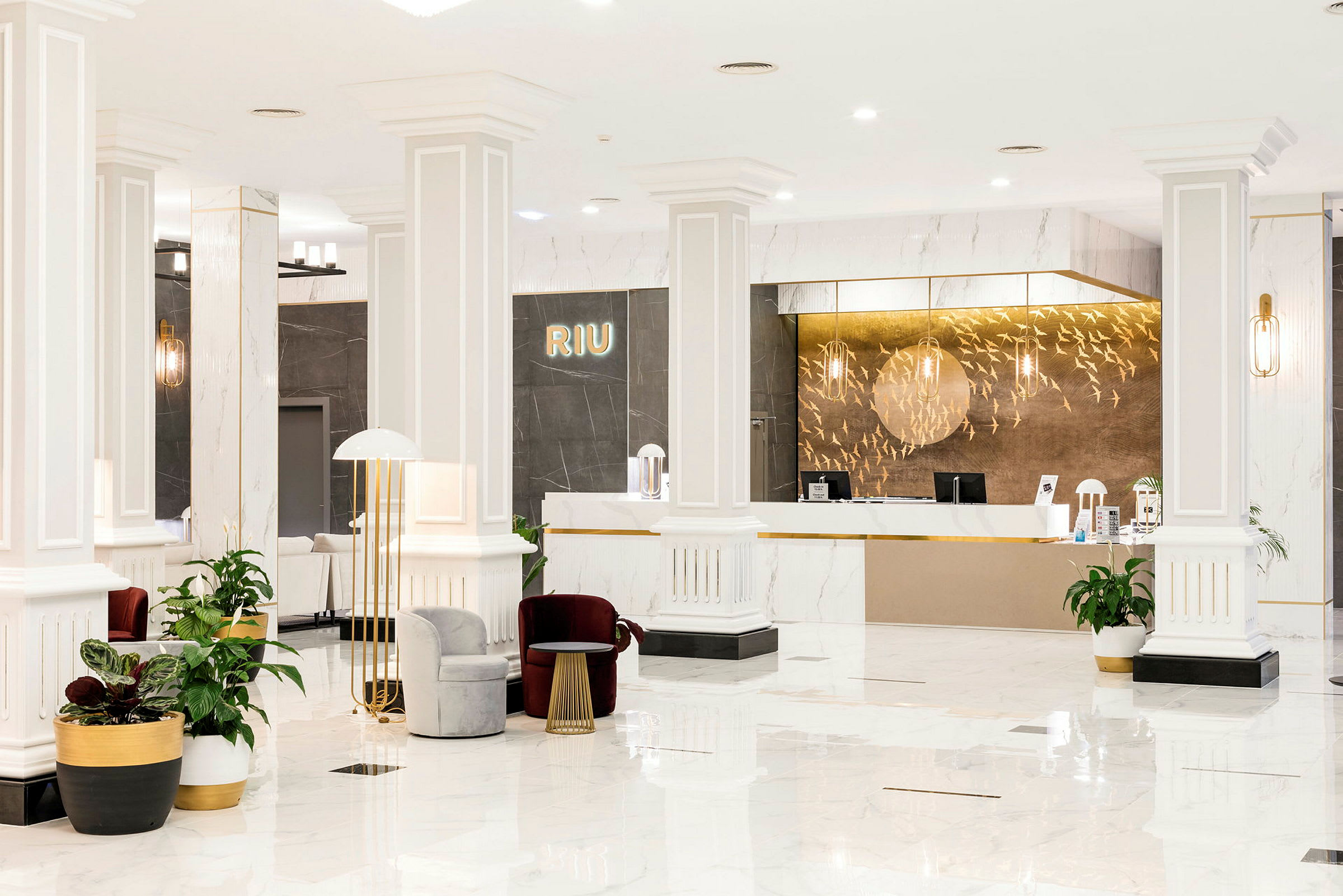 Receptionen på et Riu-hotel, moderne indrettet med hvide søjler, gulv i lys marmor og elegante møbler. (AI-genereret tekst)