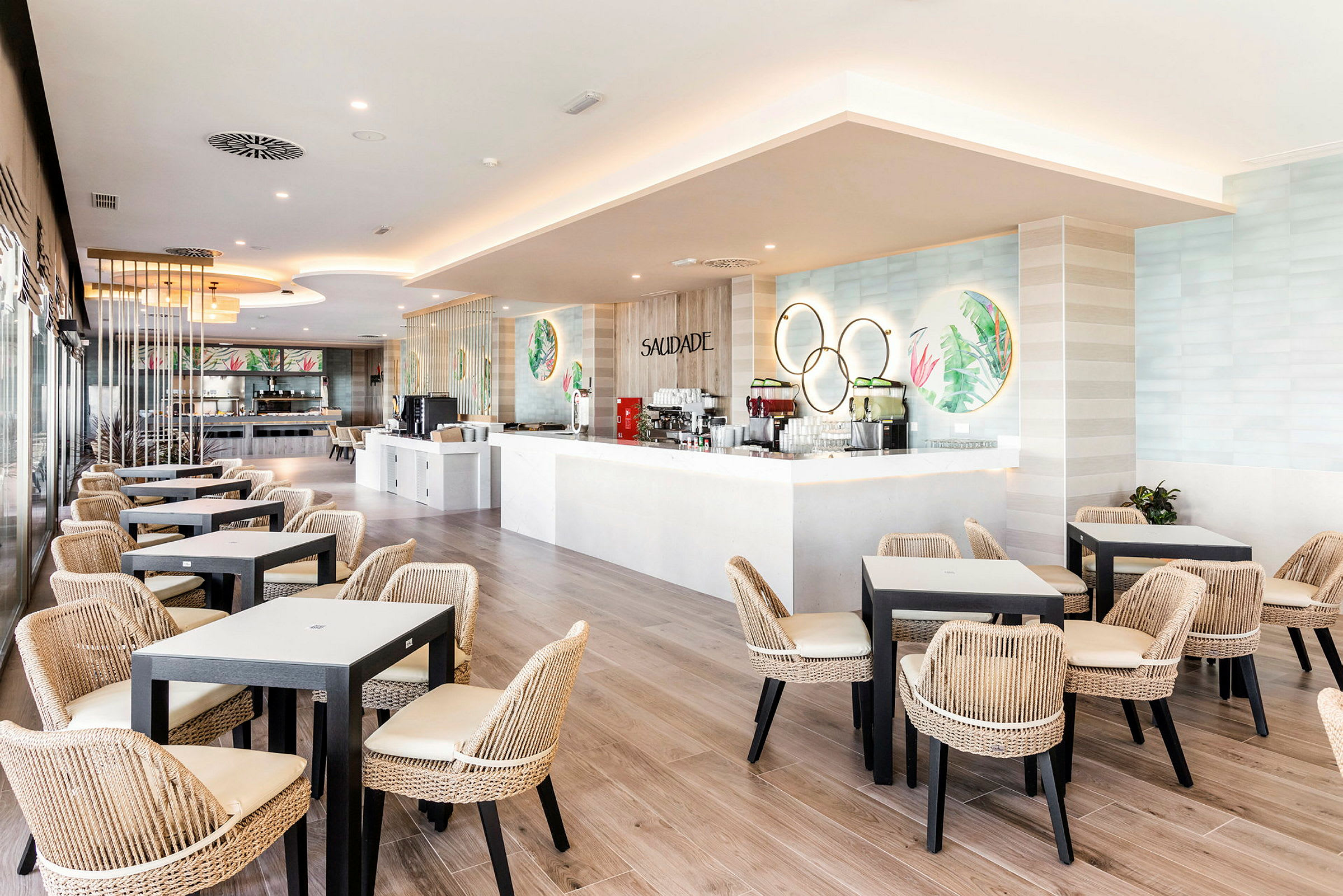 Lys restaurant med moderne borde og flettede stole samt en hvid bardisk. (AI-genereret tekst)