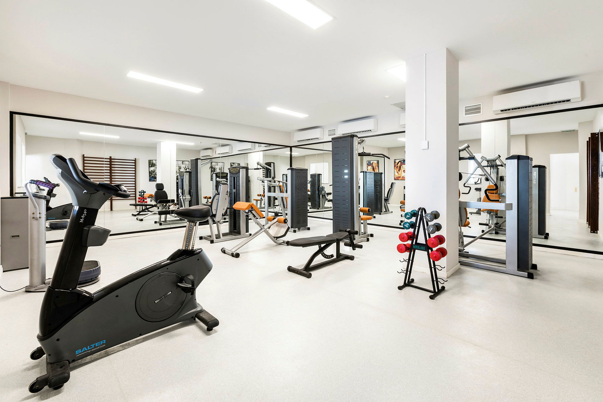 Fitnesscenter med træningsudstyr og spejle på væggene. (AI-genereret tekst)
