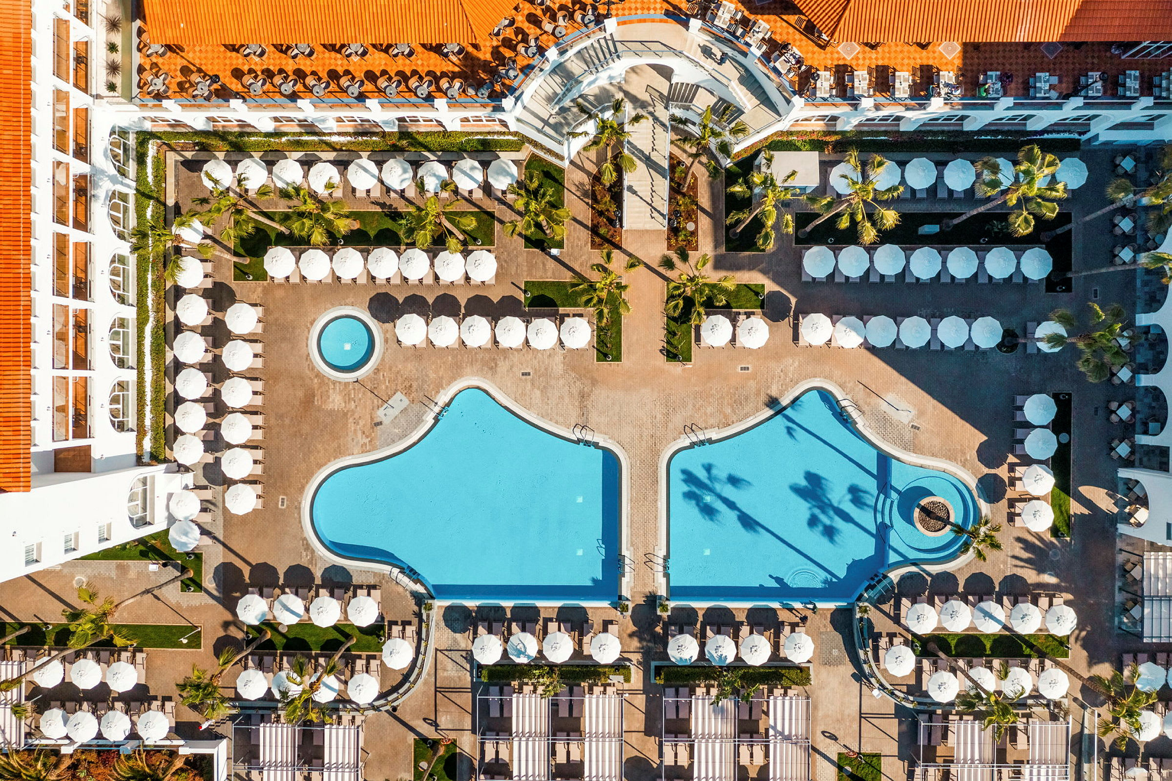 Luftfoto af hotelområde med to swimmingpools og liggestole. (AI-genereret tekst)