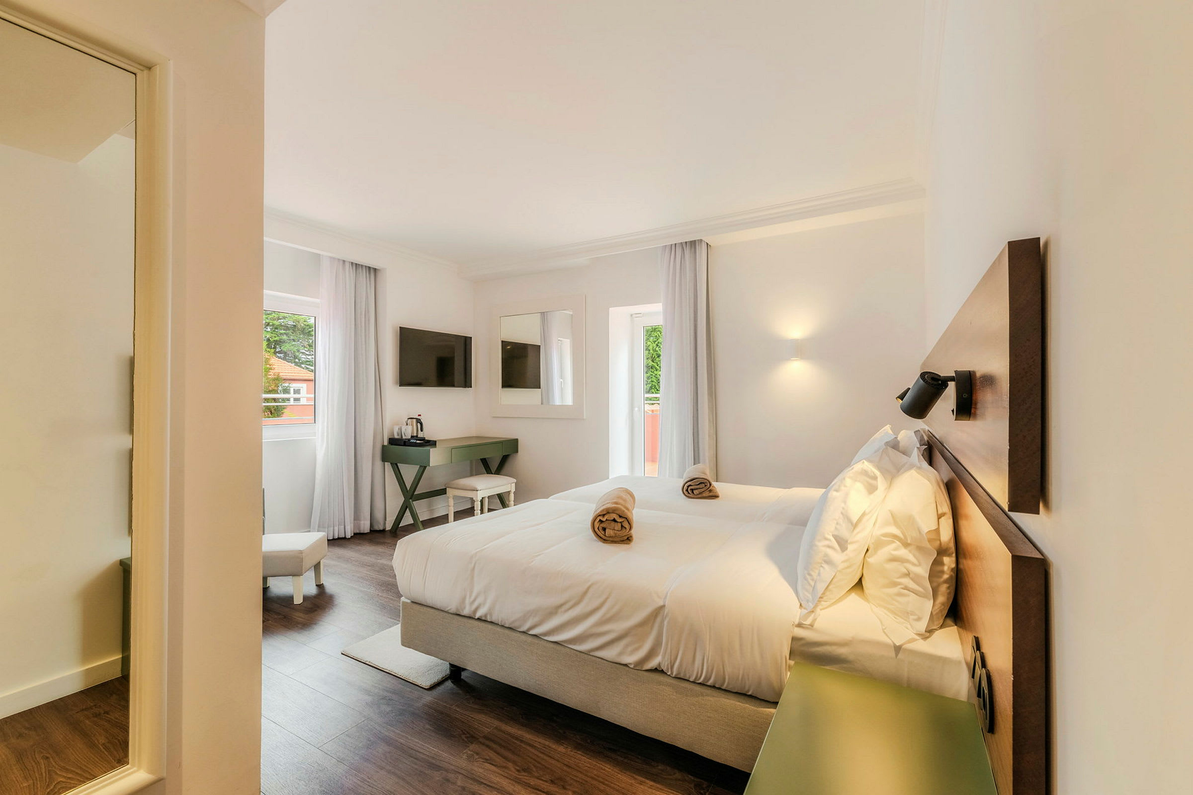 Et lyst hotelværelse med en dobbeltseng, et vindue med gardiner, et TV på væggen og et skrivebord. (AI-genereret tekst)