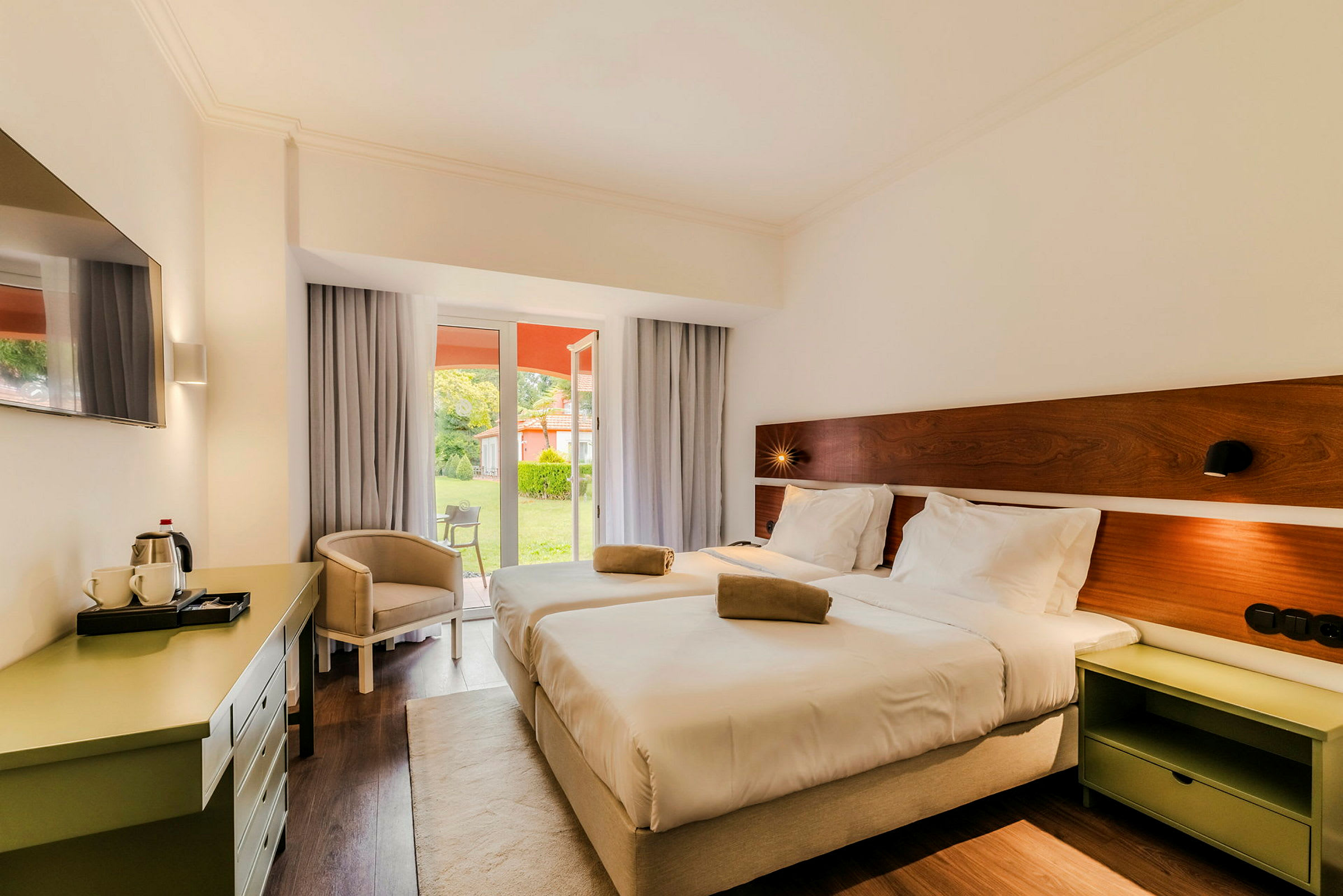 Hotelværelse med to senge overfor en vinduesdør, der fører til en frodig have. (AI-genereret tekst)