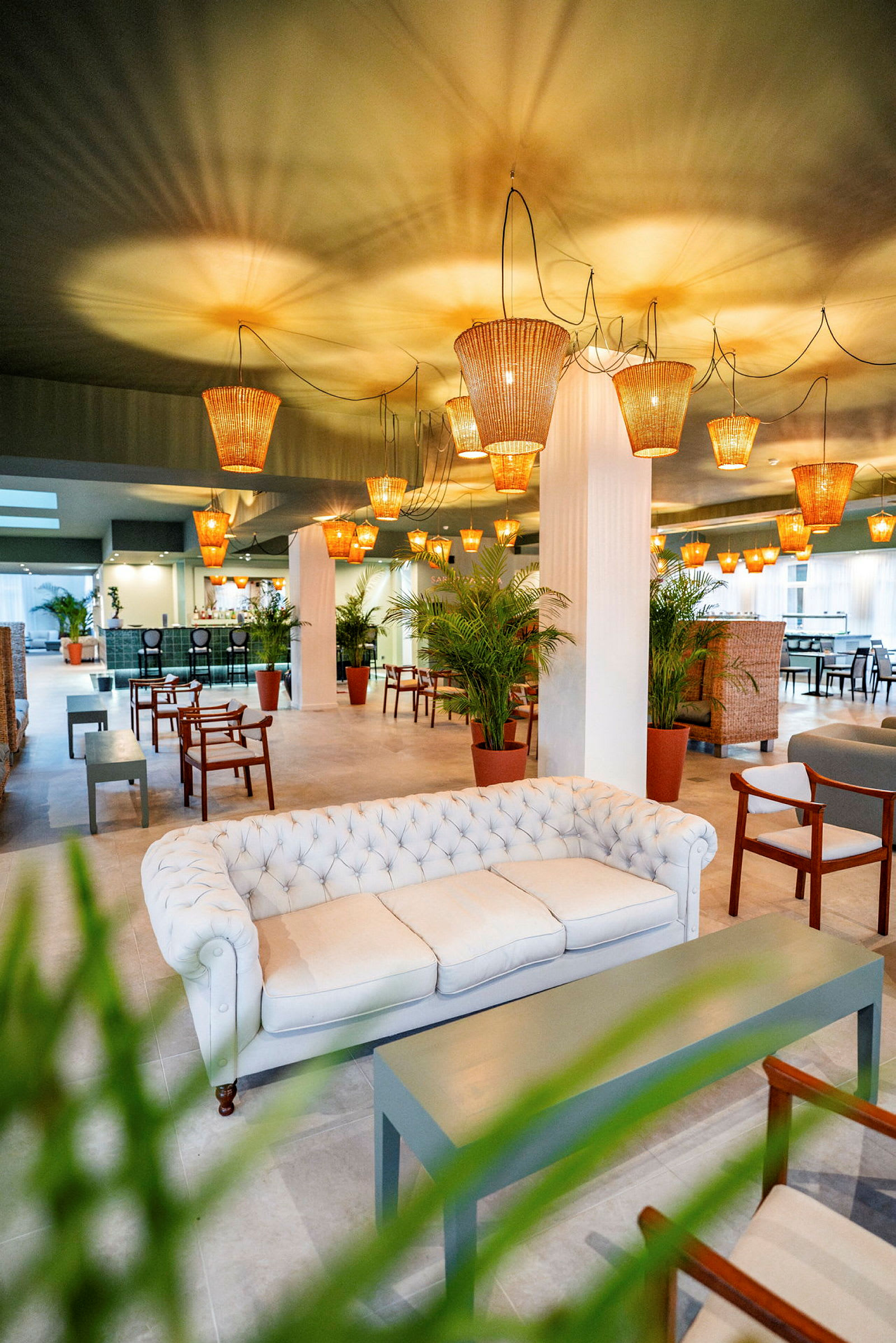 En stilfuld lounge med en hvid sofa, træmøbler, grønne planter og loftslamper af rattan. (AI-genereret tekst)
