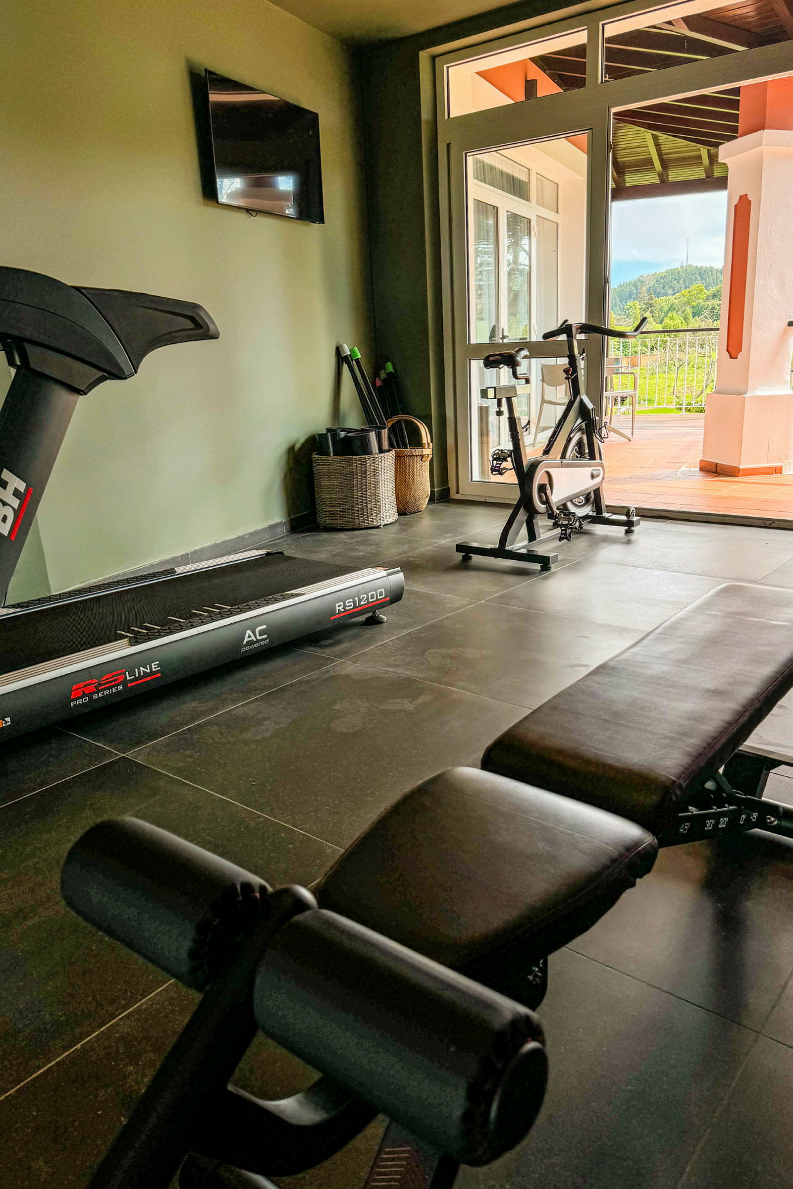 Et hjemmegym med træningsudstyr, herunder et løbebånd, en motionscykel og en bænk. (AI-genereret tekst)