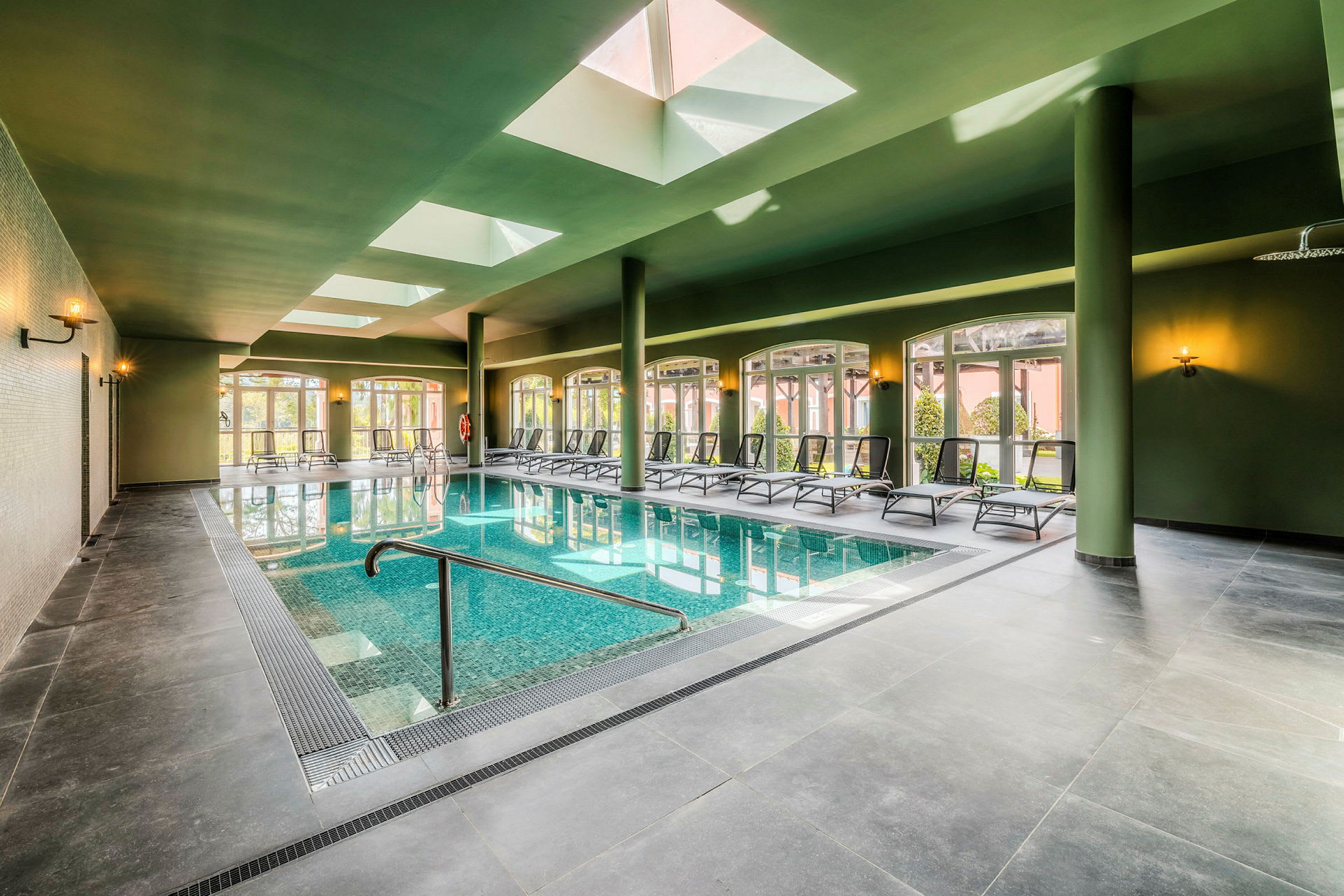 Indendørs swimmingpool med liggestole og ovenlysvinduer. (AI-genereret tekst)
