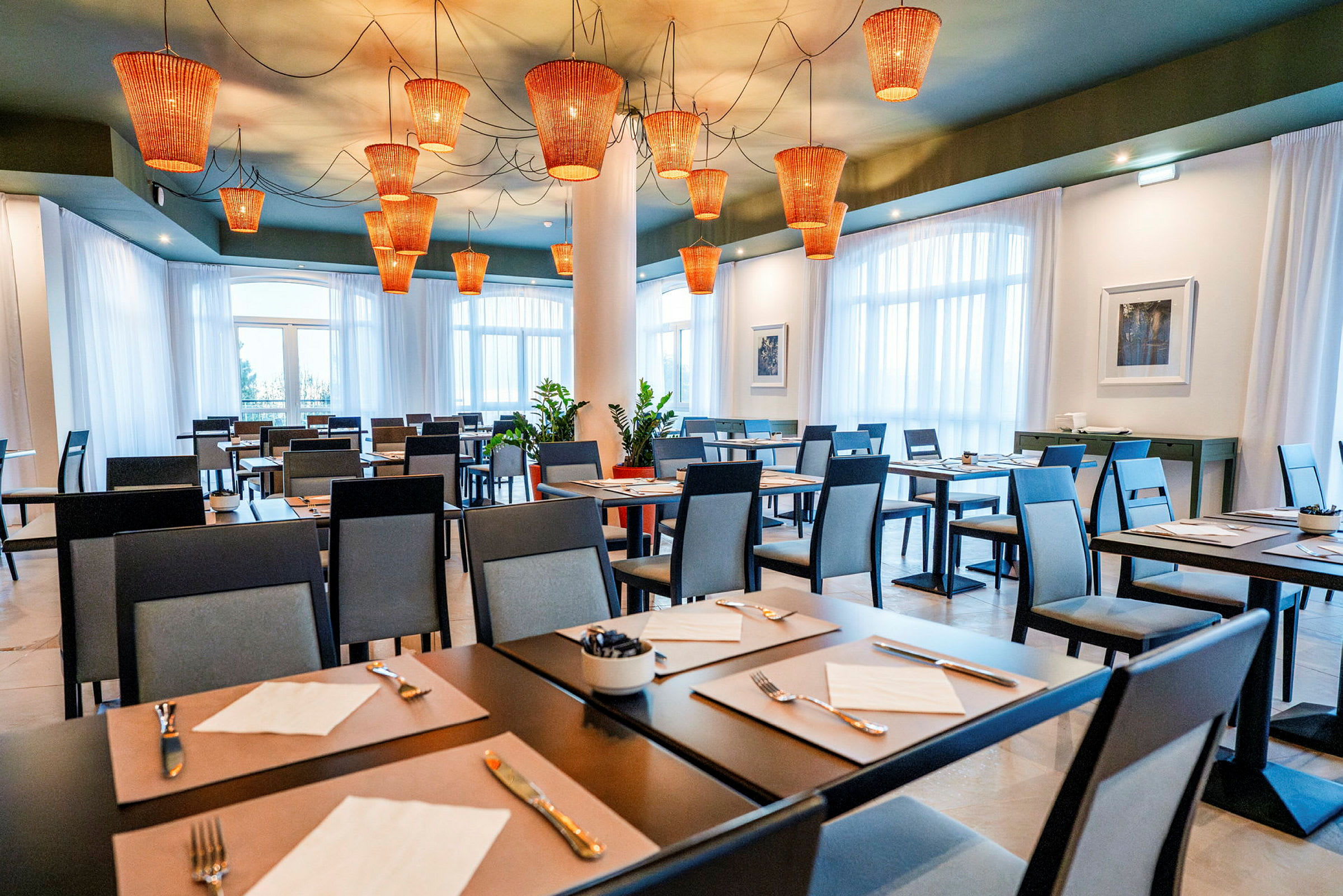 Restaurant med dækkede borde og moderne stole, med orange lamper i loftet. (AI-genereret tekst)