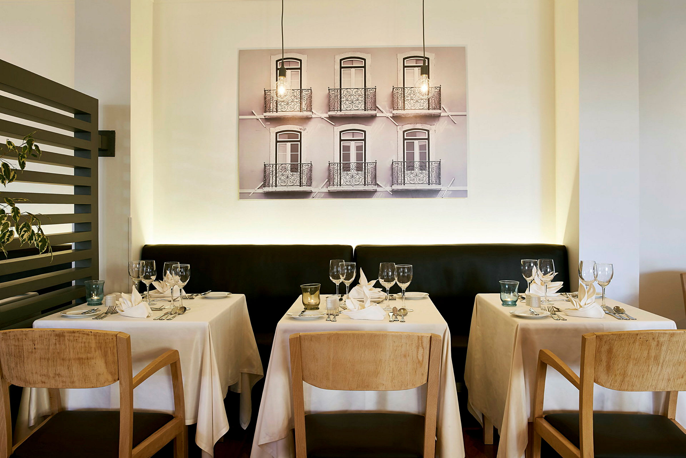 Restaurationsbordene er dækket med hvide duge, glas og porcelæn foran en væg med et stort maleri. (AI-genereret tekst)