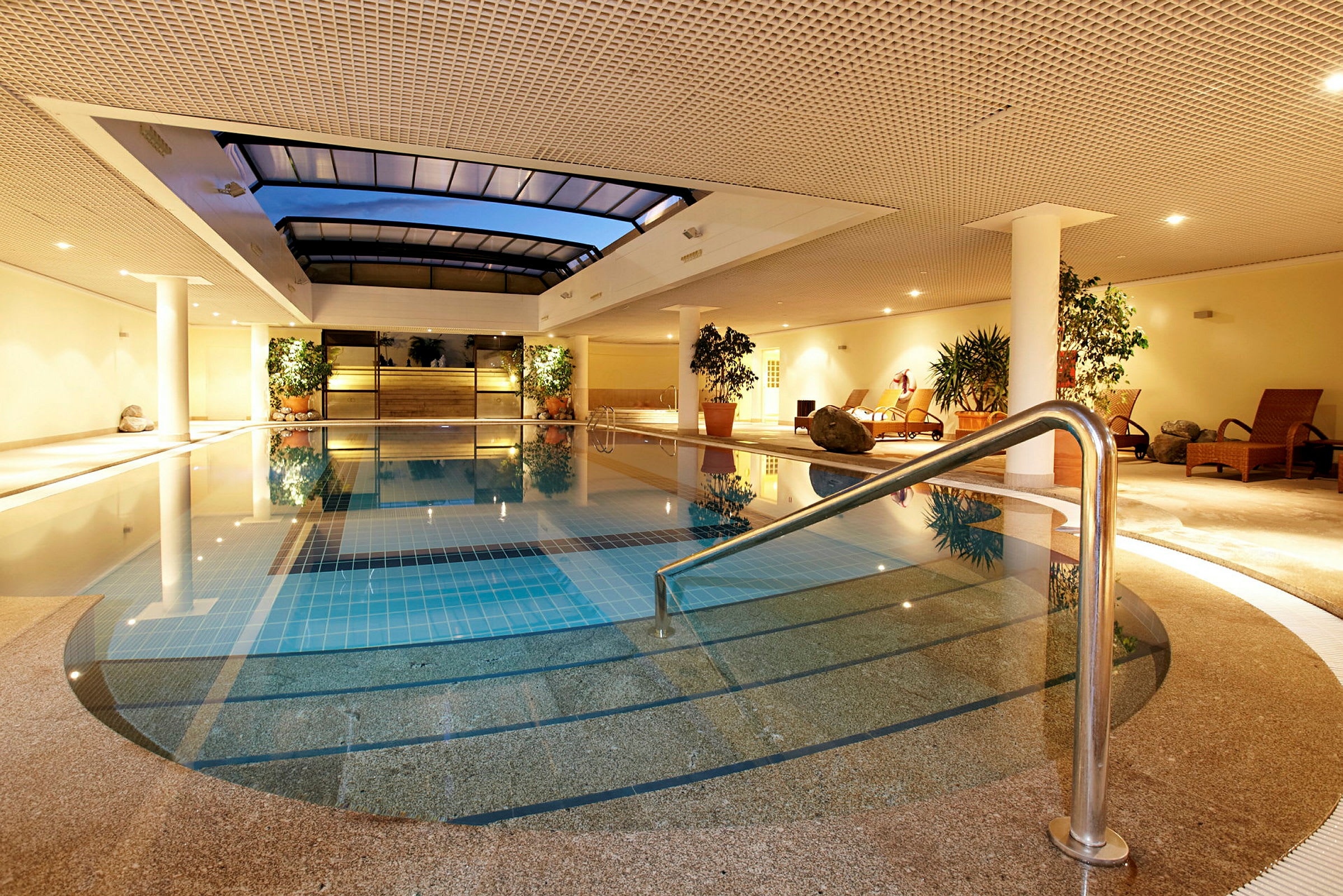 Indendørs pool med afslapningsområde indrett med liggestole og planter. (AI-genereret tekst)