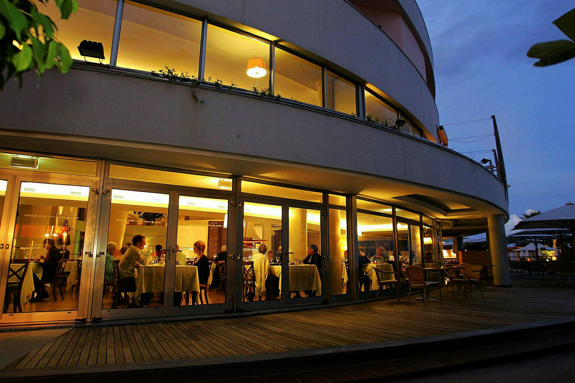 En restaurant med store glasvinduer, hvor personer kan ses samlet ved borde til middag. (AI-genereret tekst)