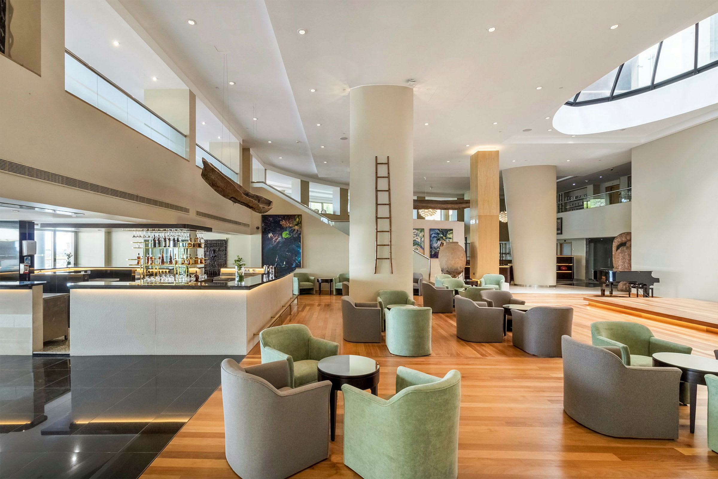 Et moderne rum med en afslappet lounge og barområde. Lænestole og borde er placeret på et trægulv, mens en bar og unikke kunstværker ses i baggrunden. (AI-genereret tekst)