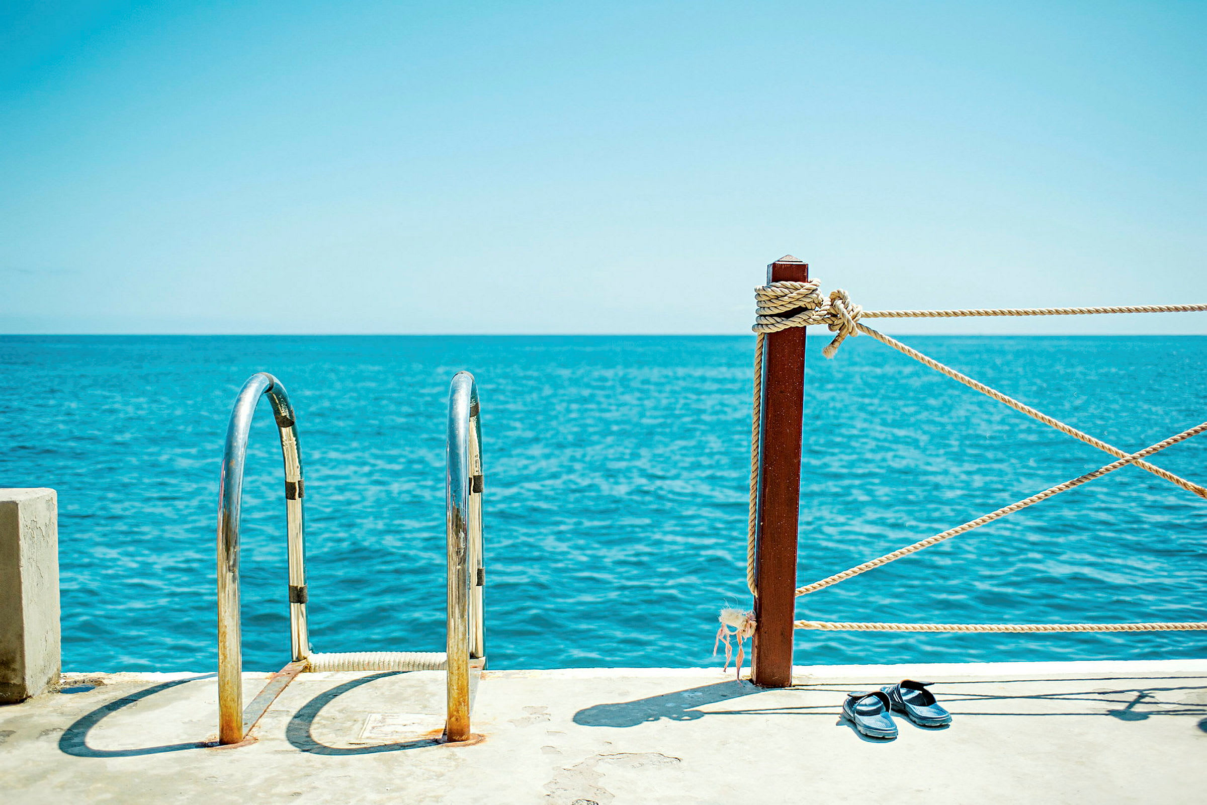 Metallstige og hegn ved havet med sandaler på jorden. (AI-genereret tekst)