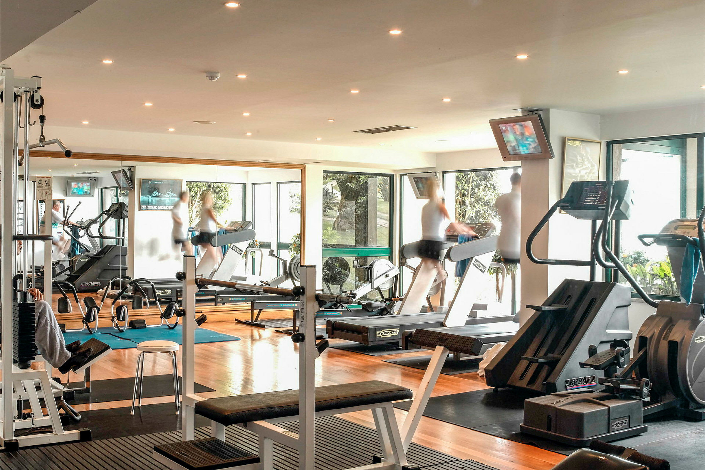 Billede af et træningscenter med forskellige fitnessmaskiner og personer, der træner. (AI-genereret tekst)