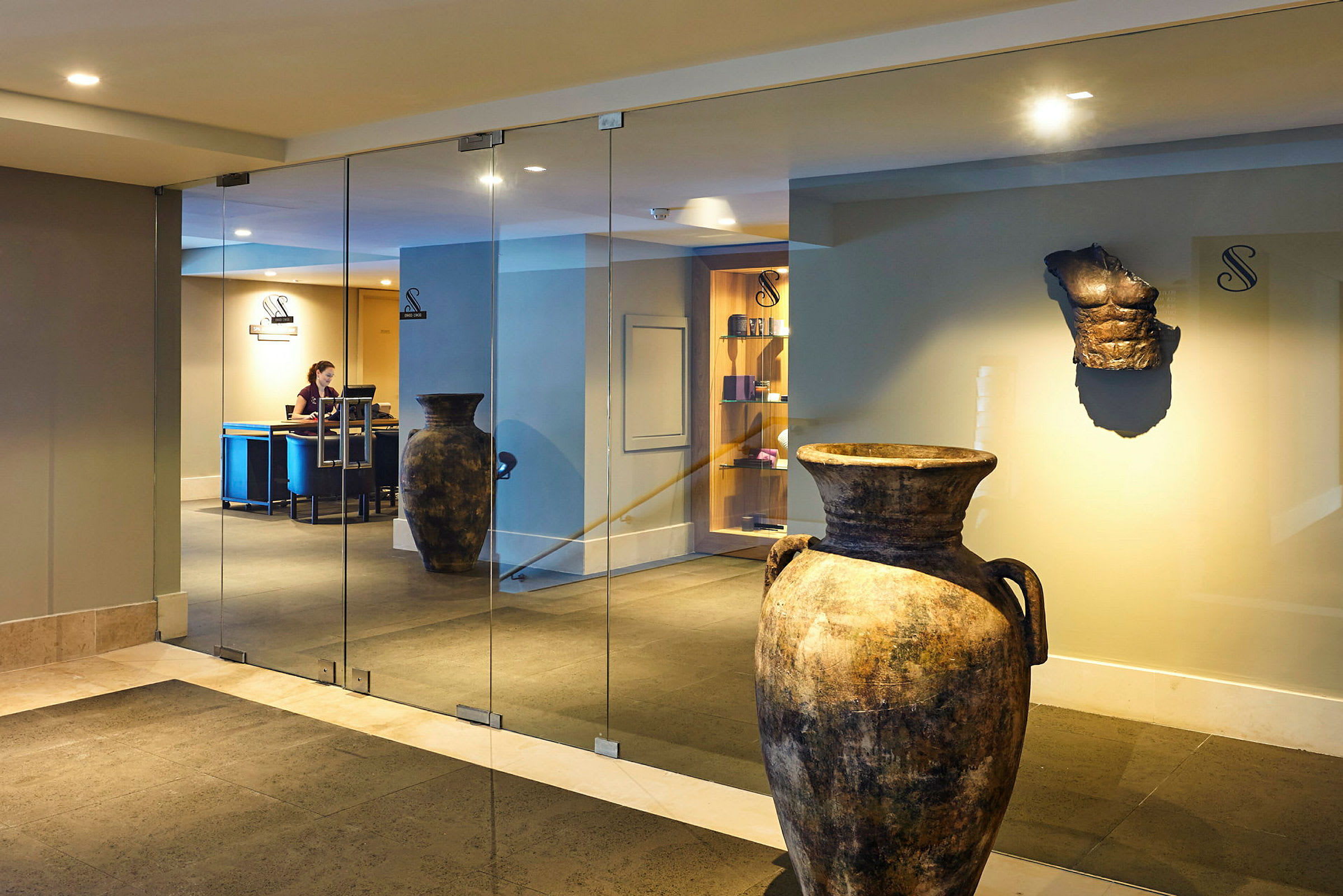 Keramikkrukker og en antik skulptur i en hotellobby med glasvægge. (AI-genereret tekst)