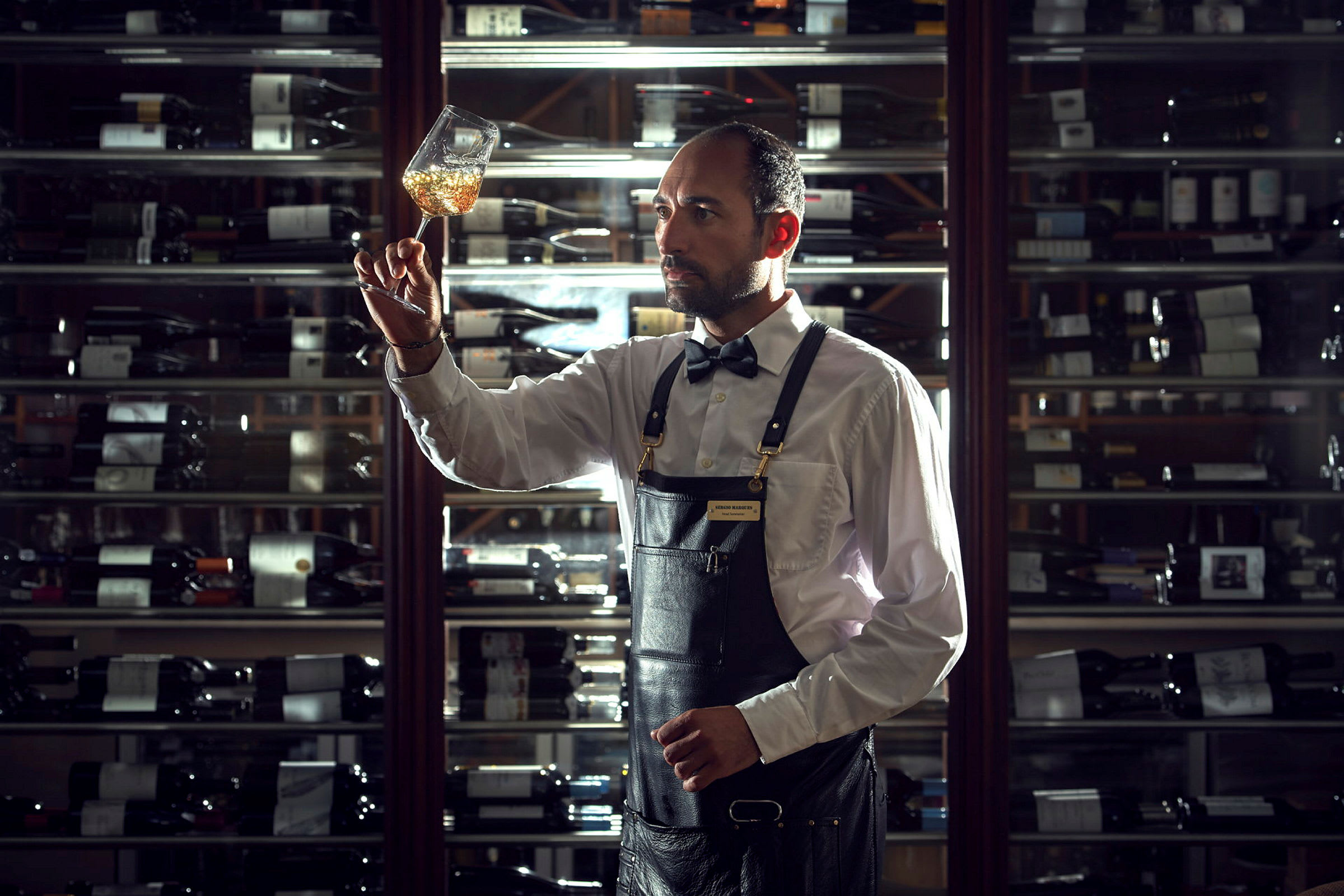 Bartender undersøger indholdet af et vinglas foran en vinhylde. (AI-genereret tekst)
