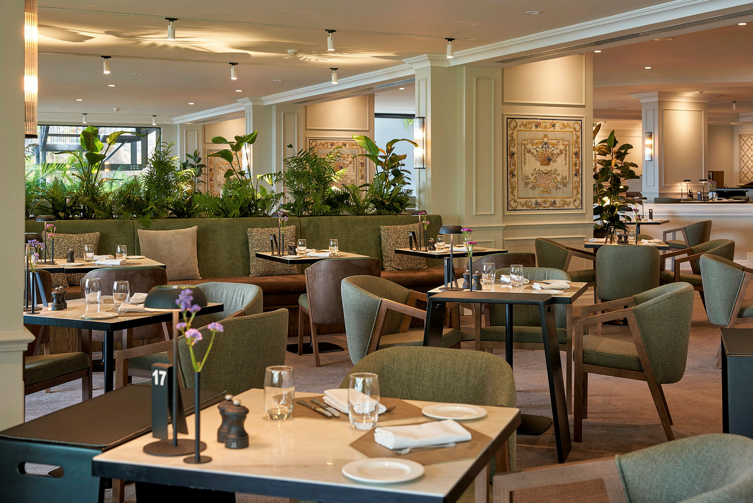 Et elegant restaurantområde med grøn indretning, borde dækket til måltider og dekorative plantearrangementer. (AI-genereret tekst)