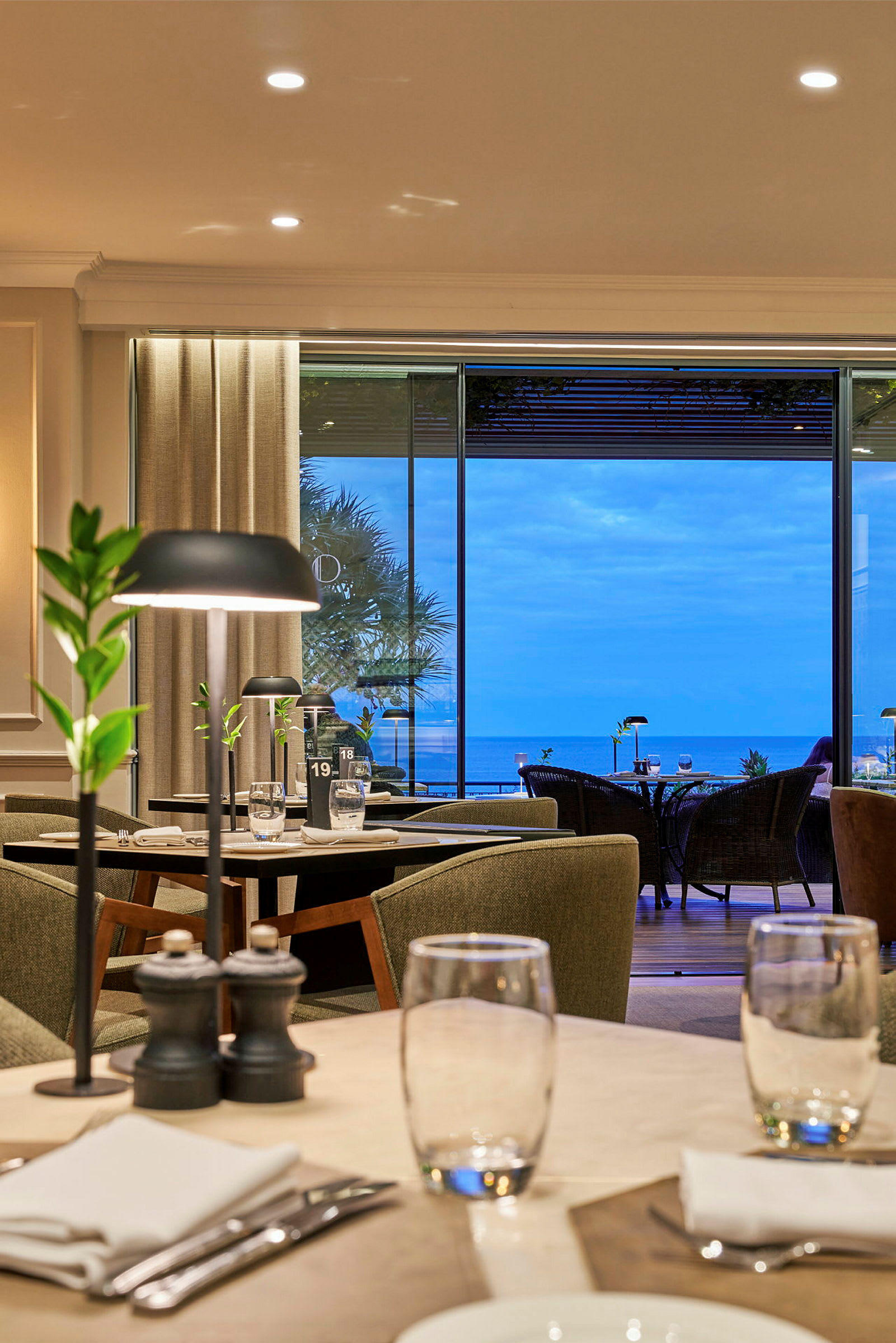 Interiør af en restaurant med dækkede borde og udsigt over havet. (AI-genereret tekst)