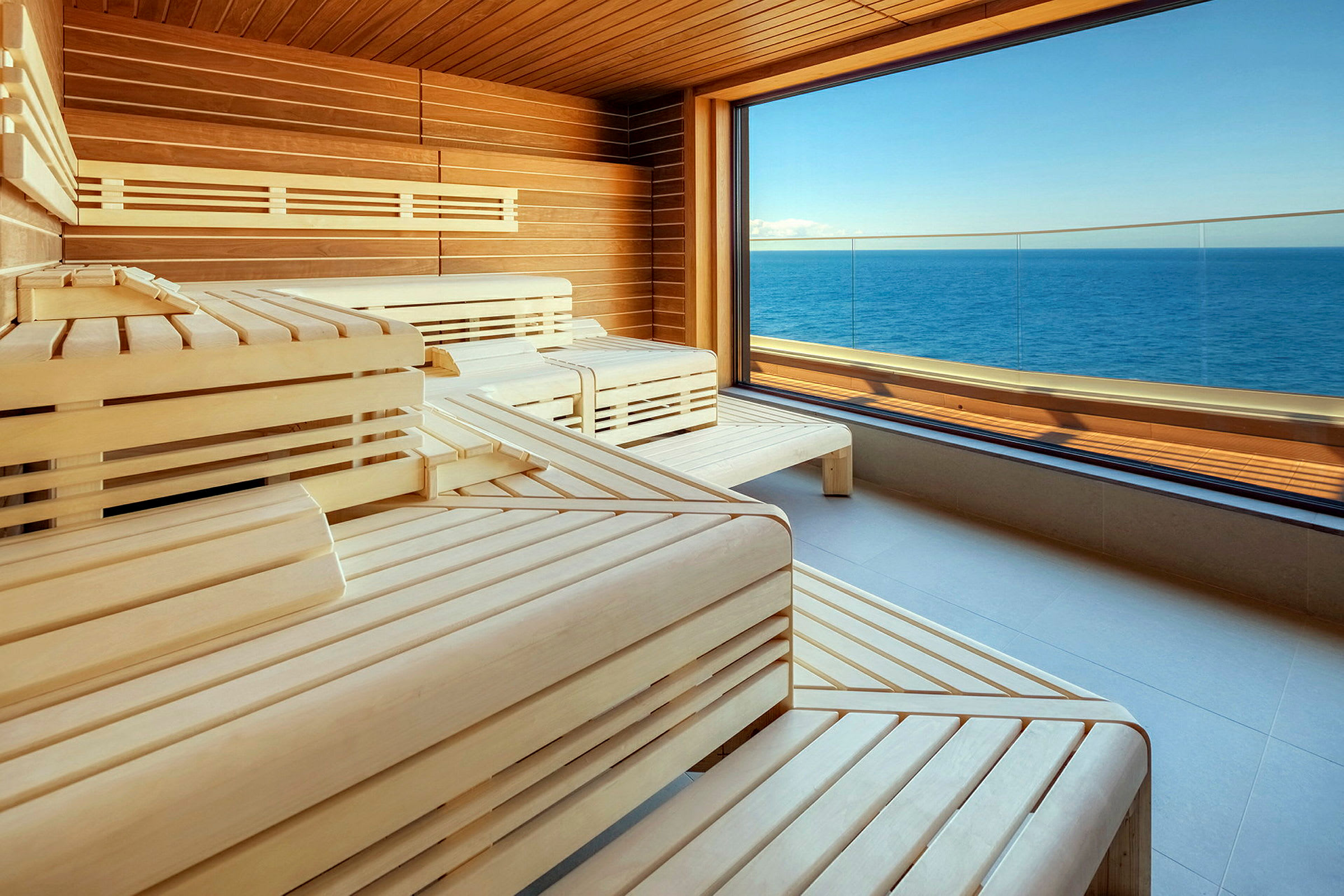 Et moderne sauna rum med træindretning og udsigt over havet gennem et stort vindue. (AI-genereret tekst)
