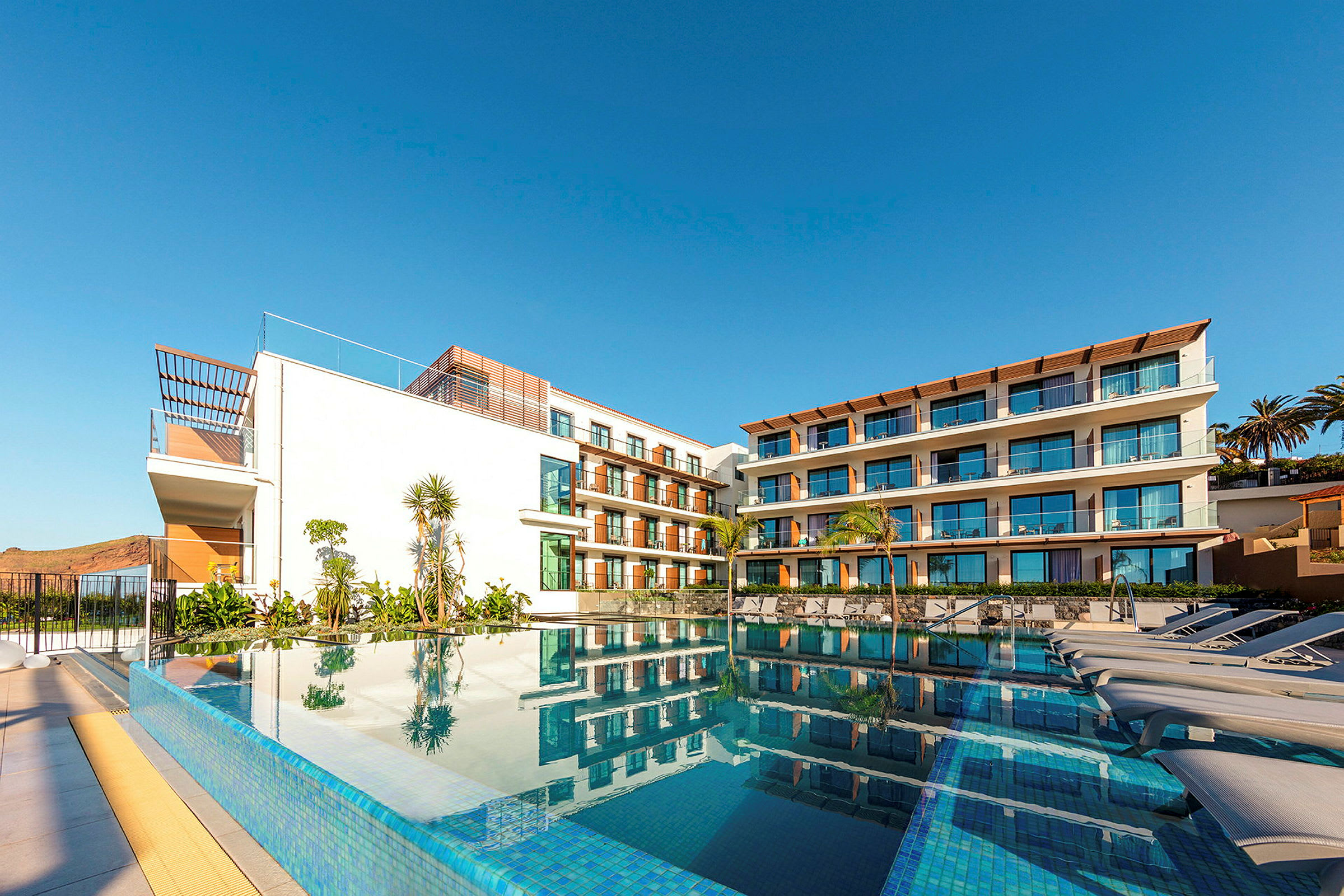 En moderne hotelbygning med store vinduer og en pool i forgrunden. (AI-genereret tekst)