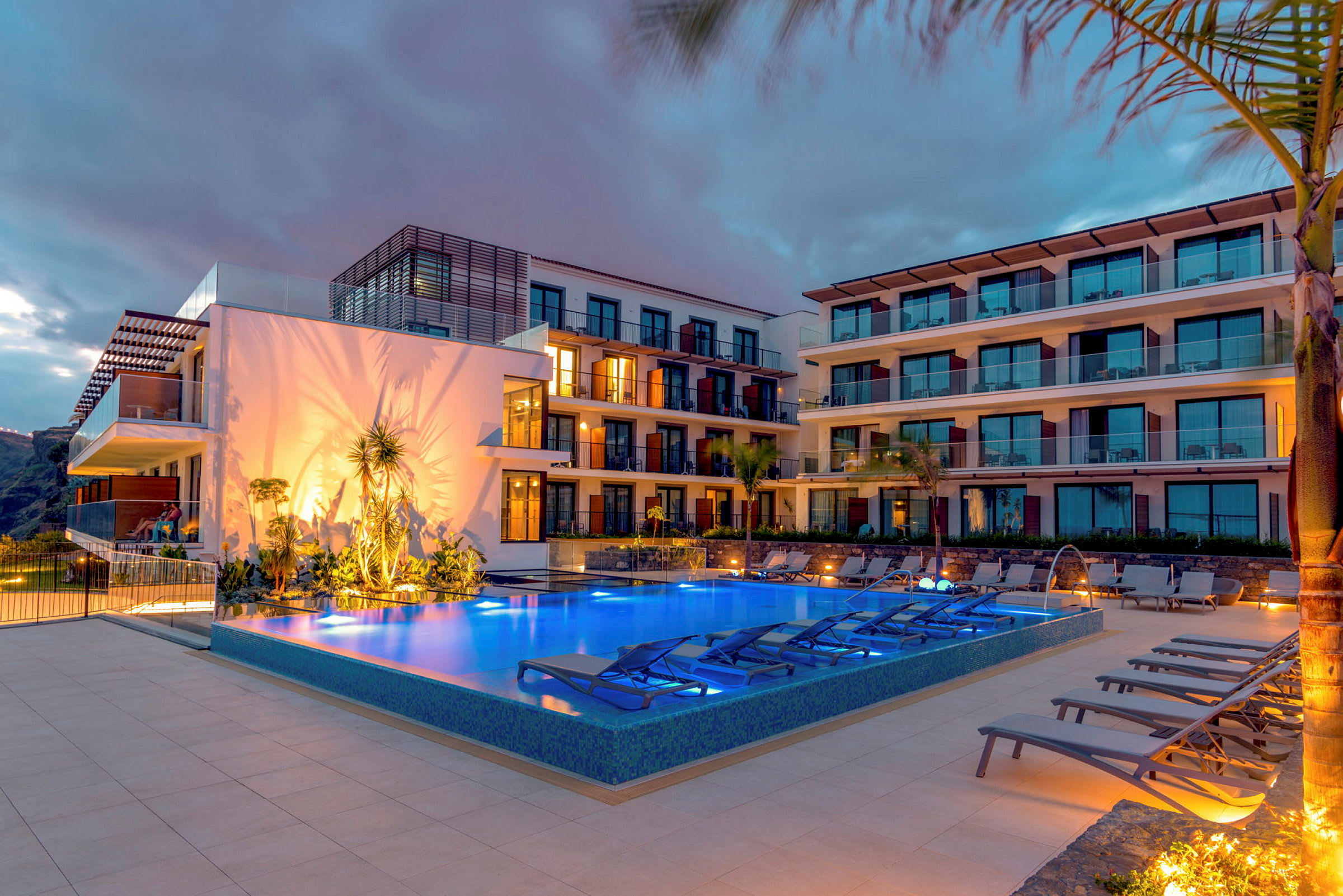 Et nattebillede af et hotel med en oplyst pool foran bygningen. (AI-genereret tekst)
