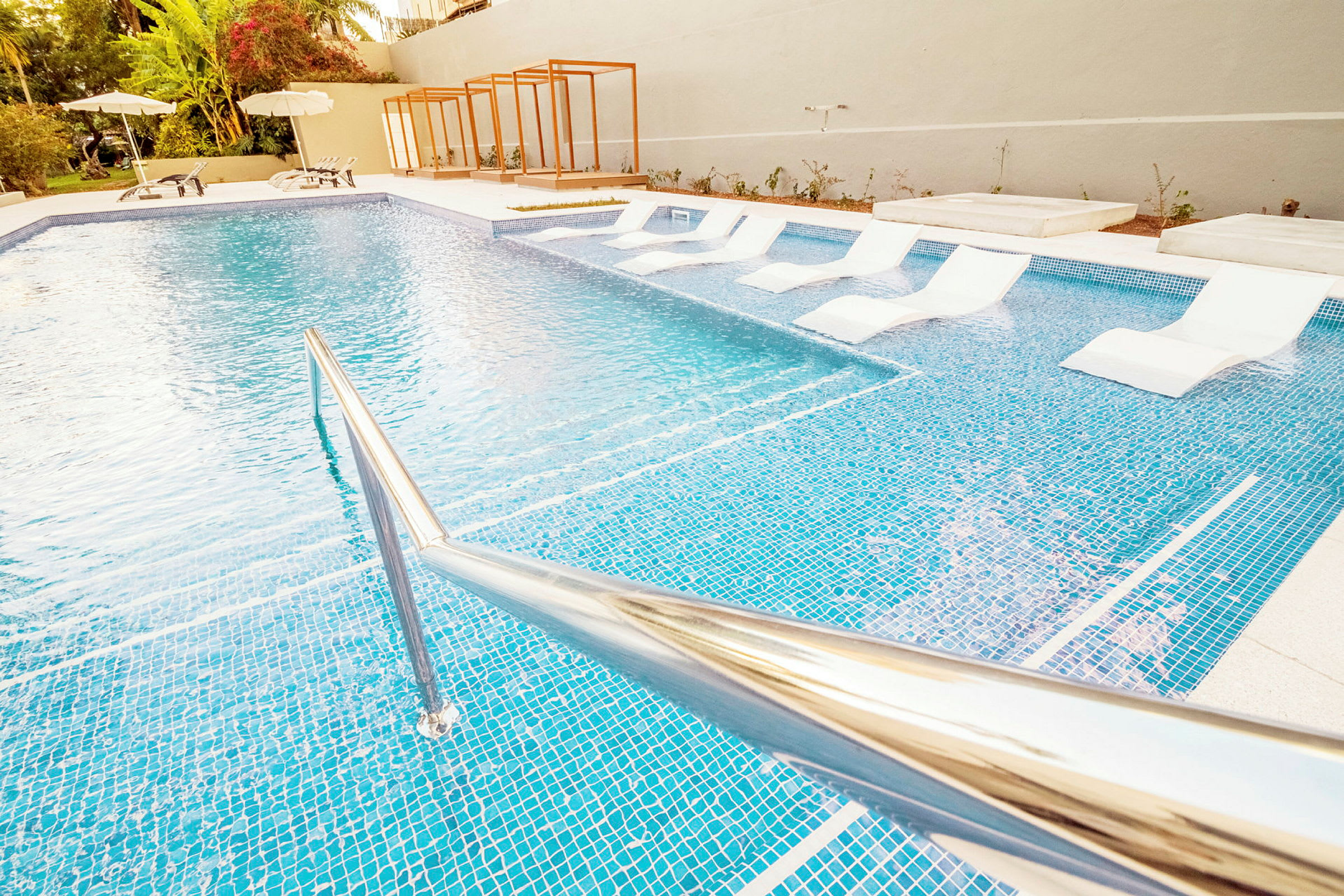 Udendørs swimmingpool med liggestole i vandet og parasoller ved siden af. (AI-genereret tekst)
