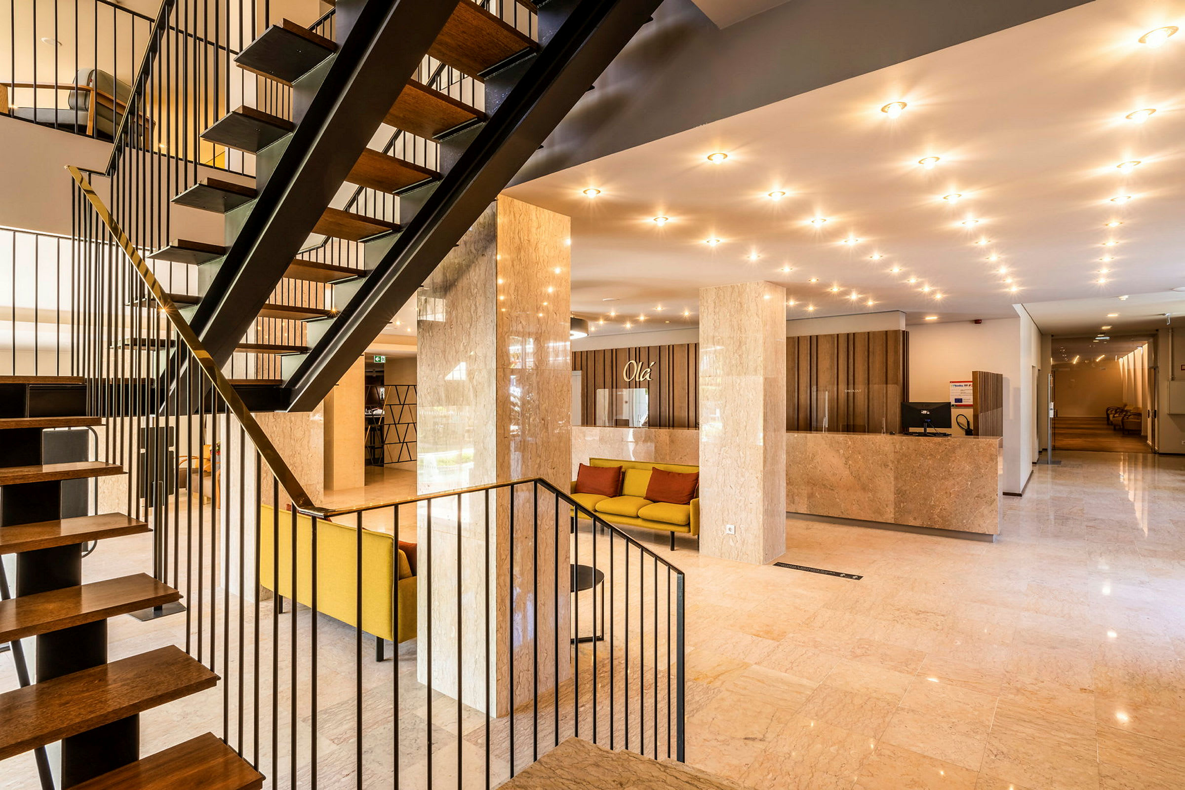 Hotellobby med en trappe, siddeområder og receptionsdisk. (AI-genereret tekst)