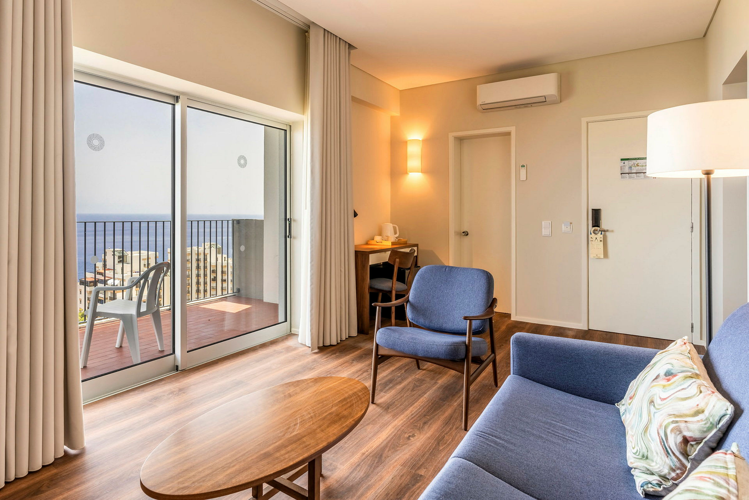 Moderne hotelværelse med siddepladser og udsigt over havet gennem store vinduer. (AI-genereret tekst)