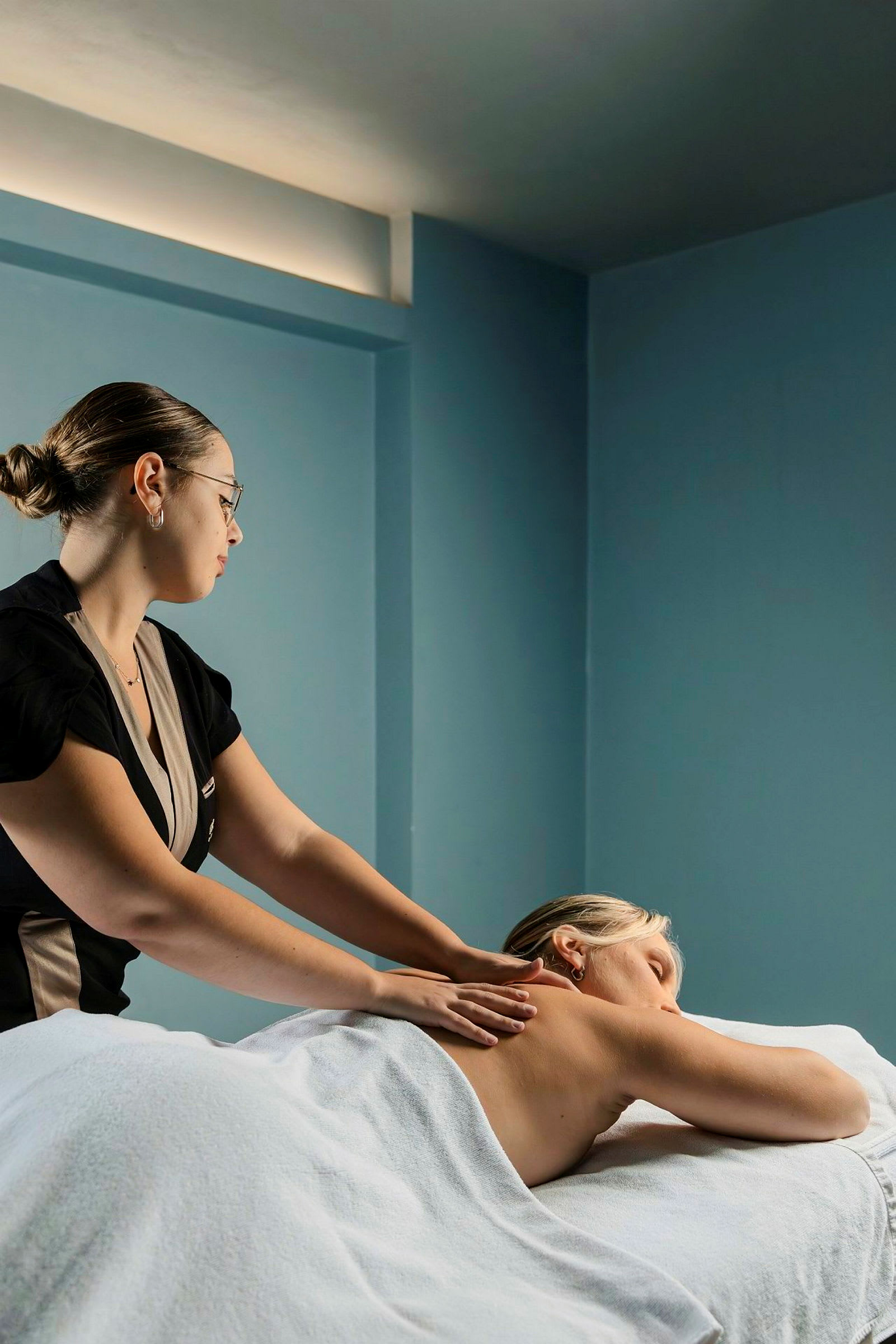 En person får en rygmassage af en massør i et rum med blå vægge. (AI-genereret tekst)