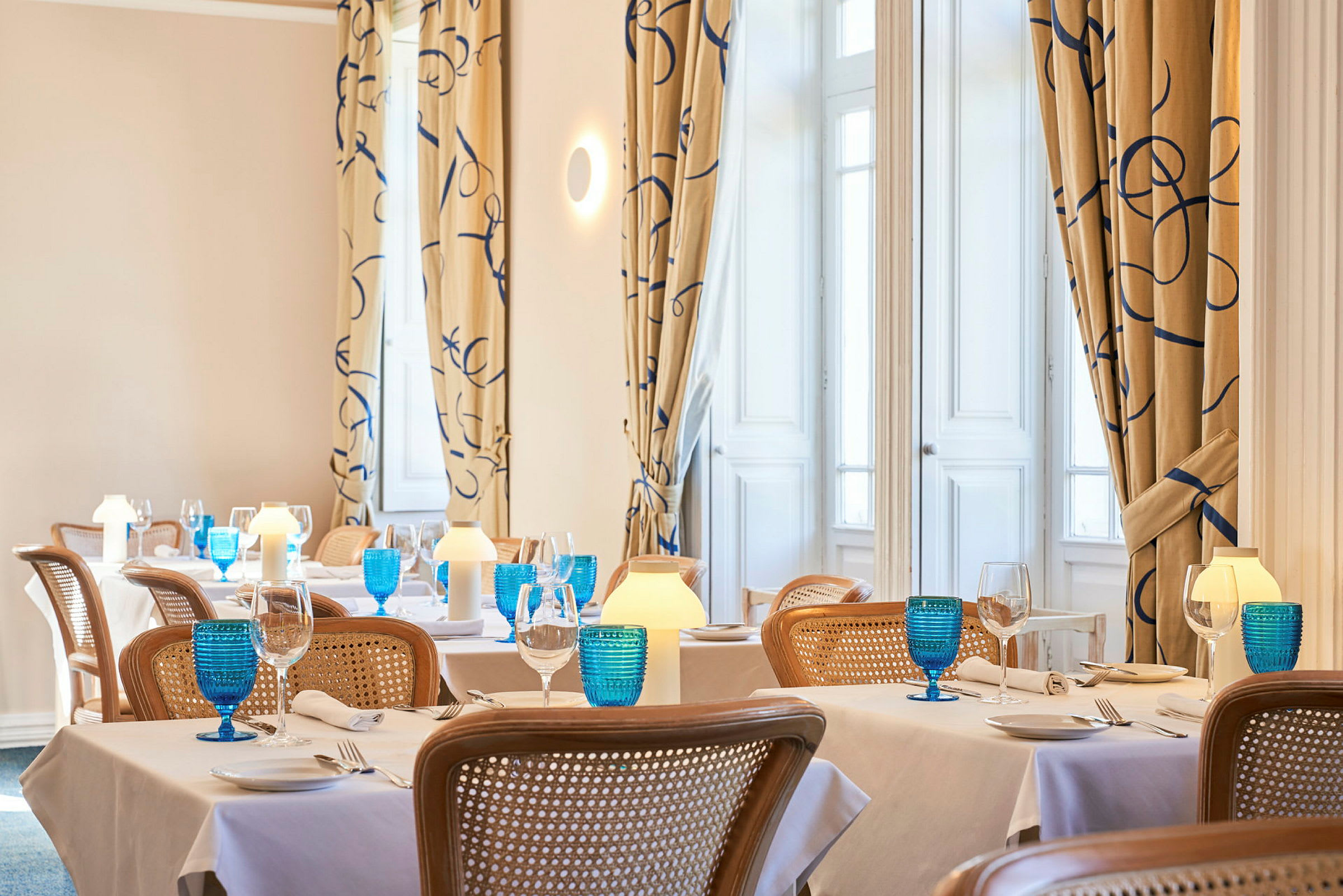 Billede af en elegant restaurant med dækkede borde, blå glas og varm belysning. (AI-genereret tekst)