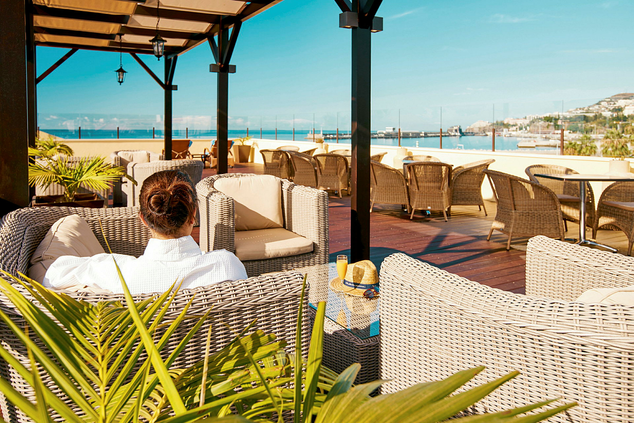 En person sidder i en flettet lænestol på en terrasse med udsigt over havet. (AI-genereret tekst)