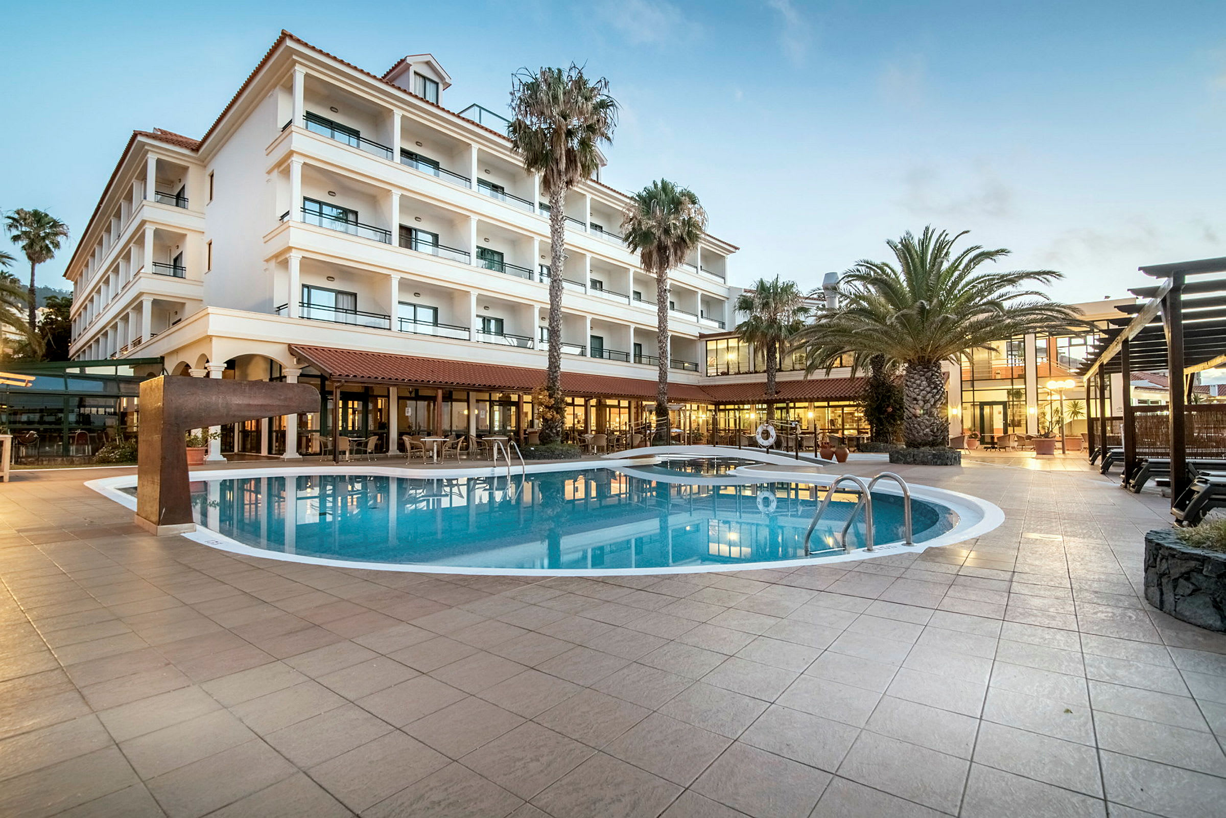 Hotel med flere etager og en udendørs pool, omgivet af palmer. (AI-genereret tekst)
