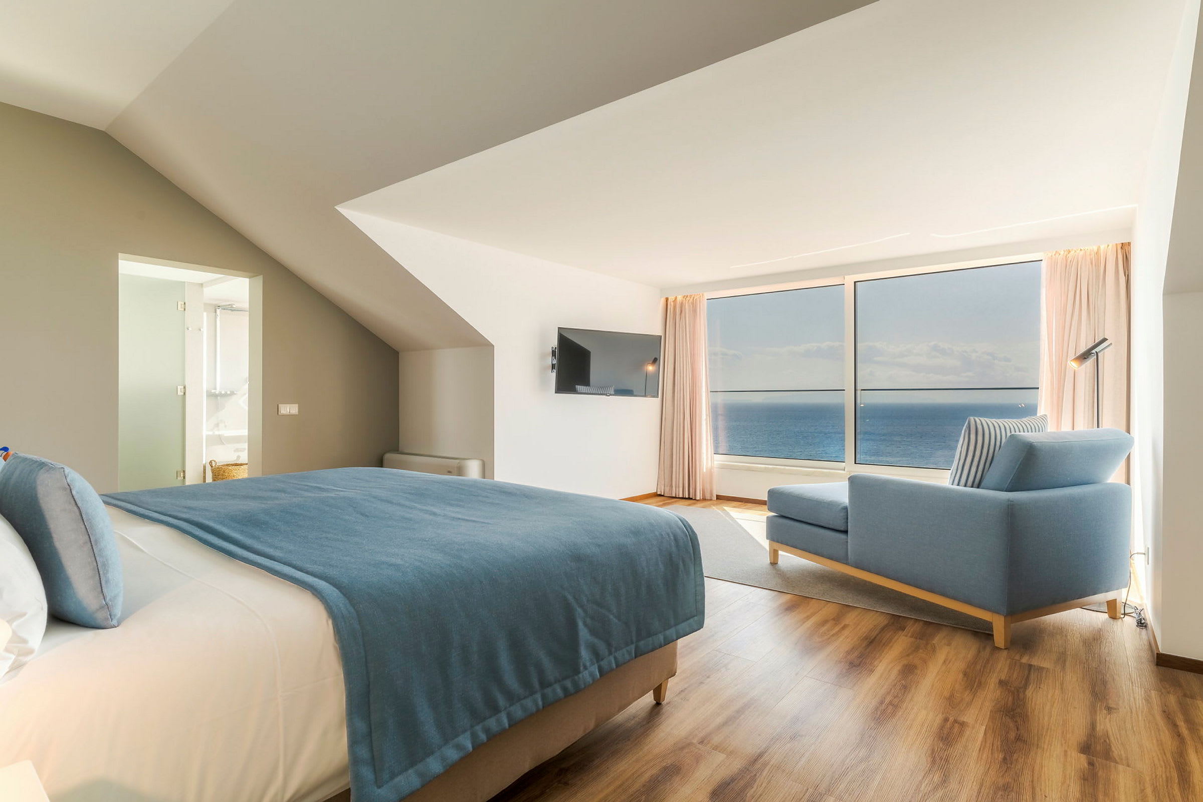 Moderne hotelværelse med havudsigt, seng med blåt sengetæppe og blå sofa. (AI-genereret tekst)