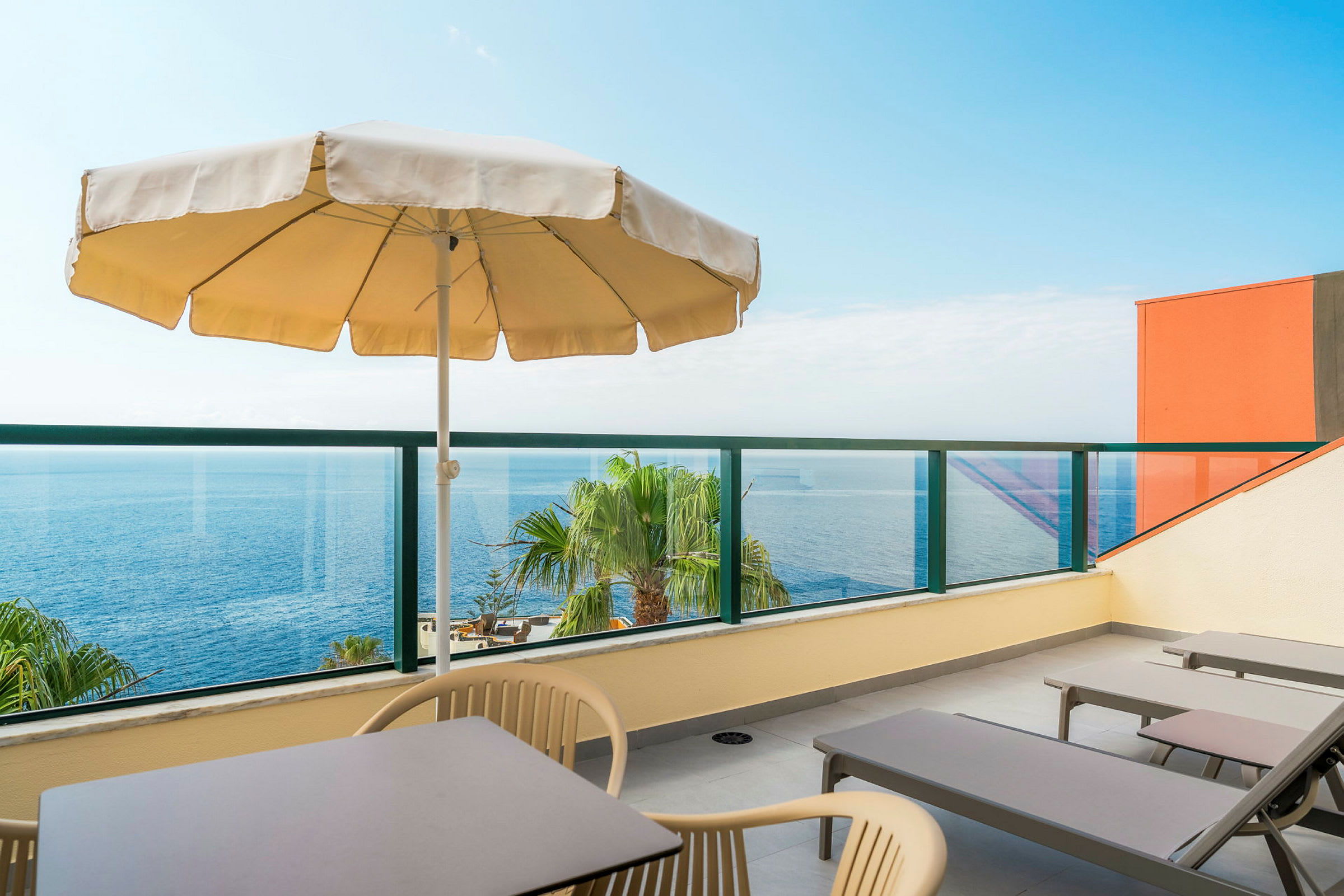 En terrasse med liggestole, bord, stole og en parasol med udsigt over havet. (AI-genereret tekst)