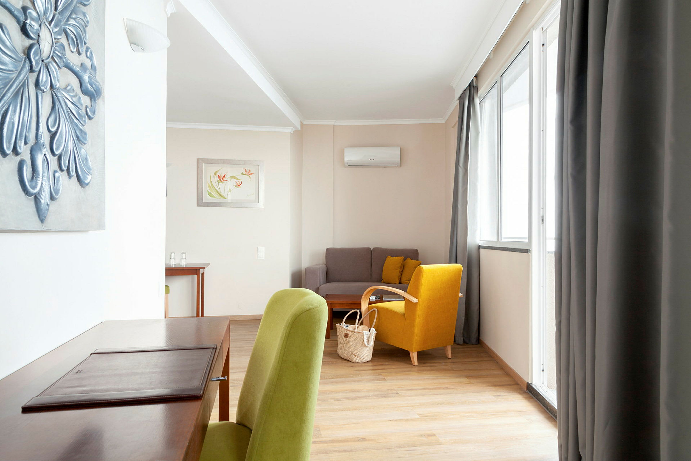 Et velindrettet opholdsrum med en grøn og en gul stol, en sofa og et skrivebord. (AI-genereret tekst)