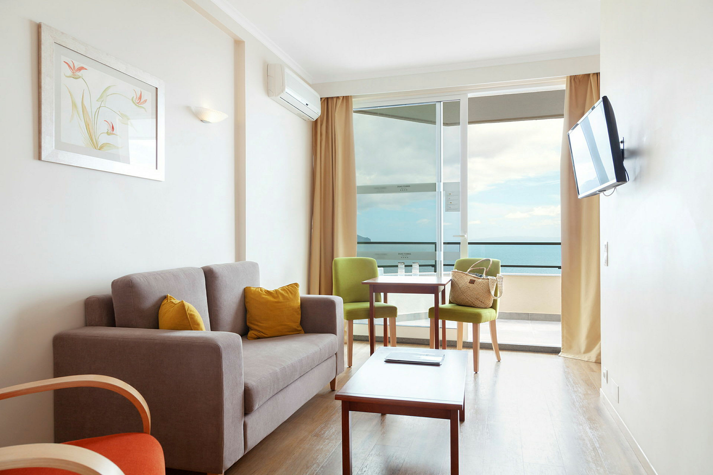 En stue med sofa, to stole, et bord og en stor altan med udsigt over havet. (AI-genereret tekst)