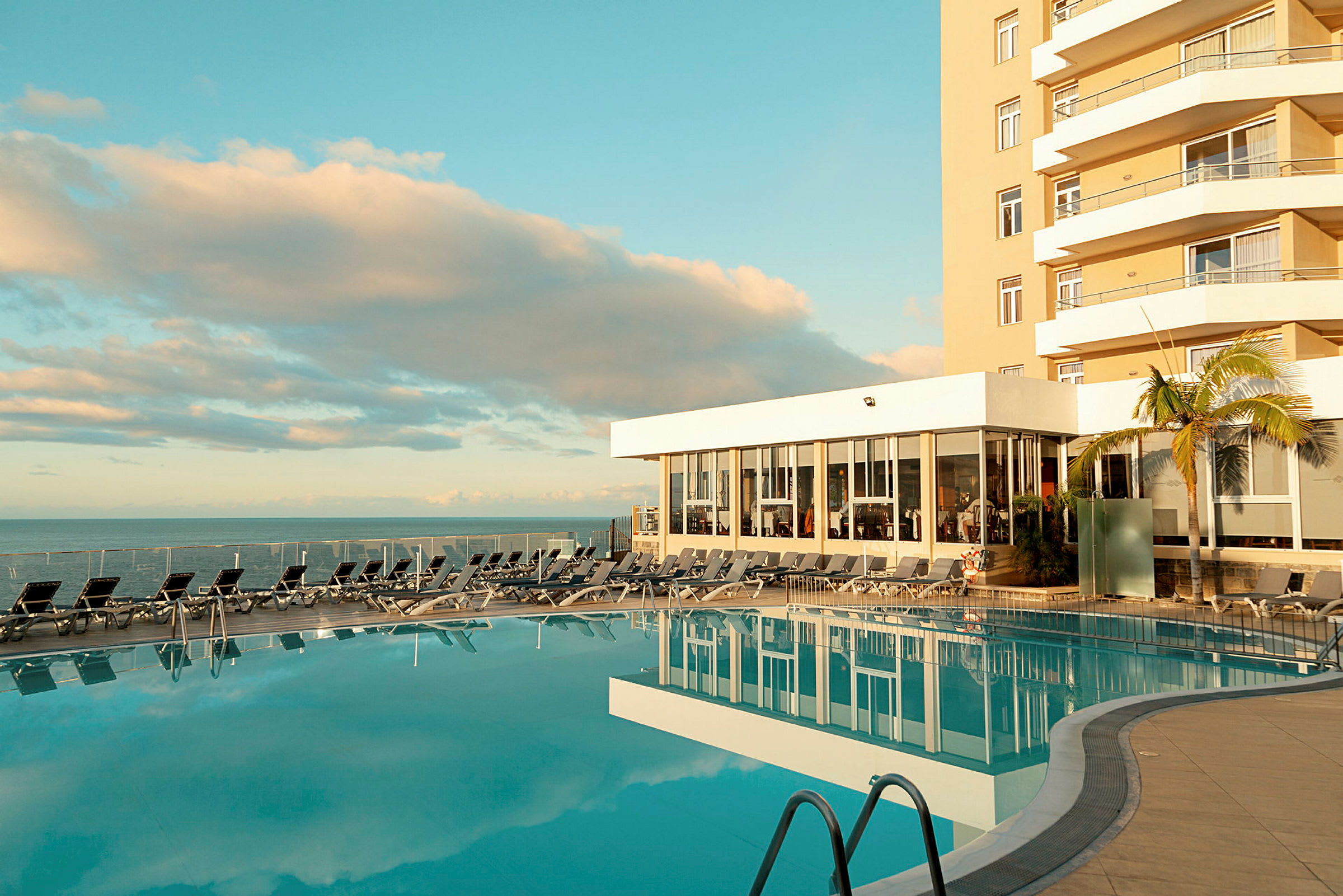 Udendørs pool ved hotel med liggestole og havudsigt. (AI-genereret tekst)