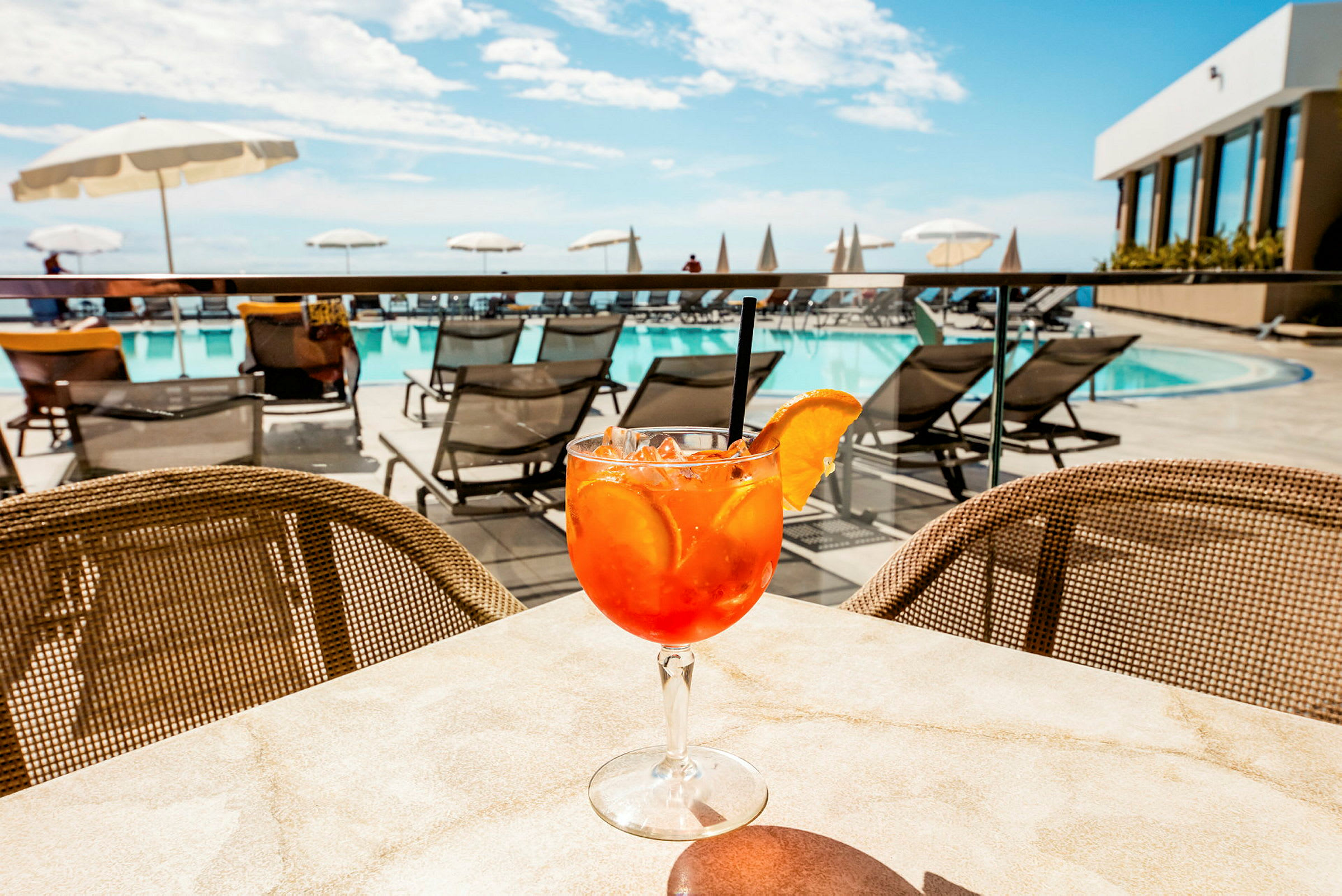 Et glas med en orange drik dekoreret med en appelsinskive på et bord nær en pool. (AI-genereret tekst)