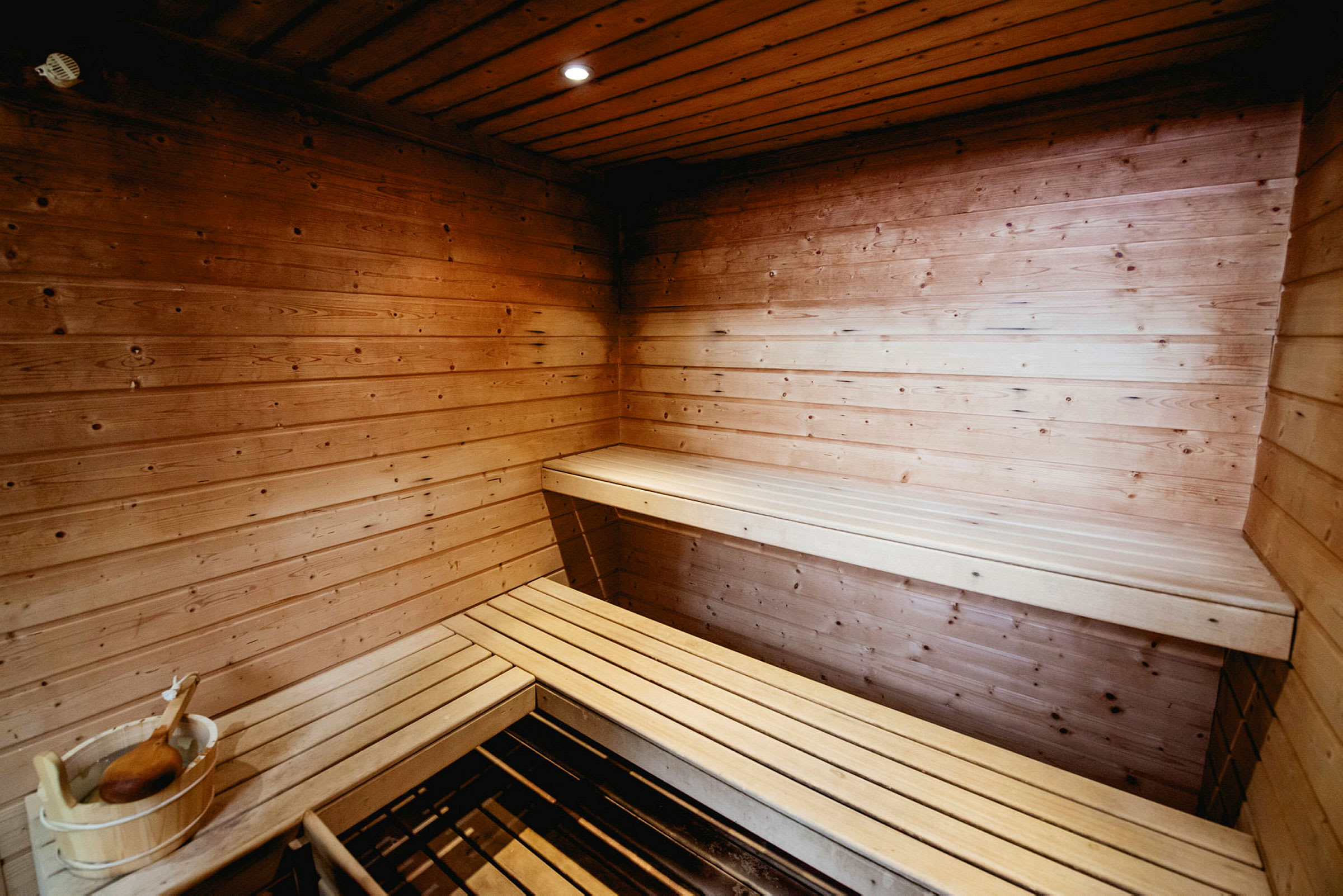 En træbeklædt sauna med siddebænke og en træspand med en øse. (AI-genereret tekst)