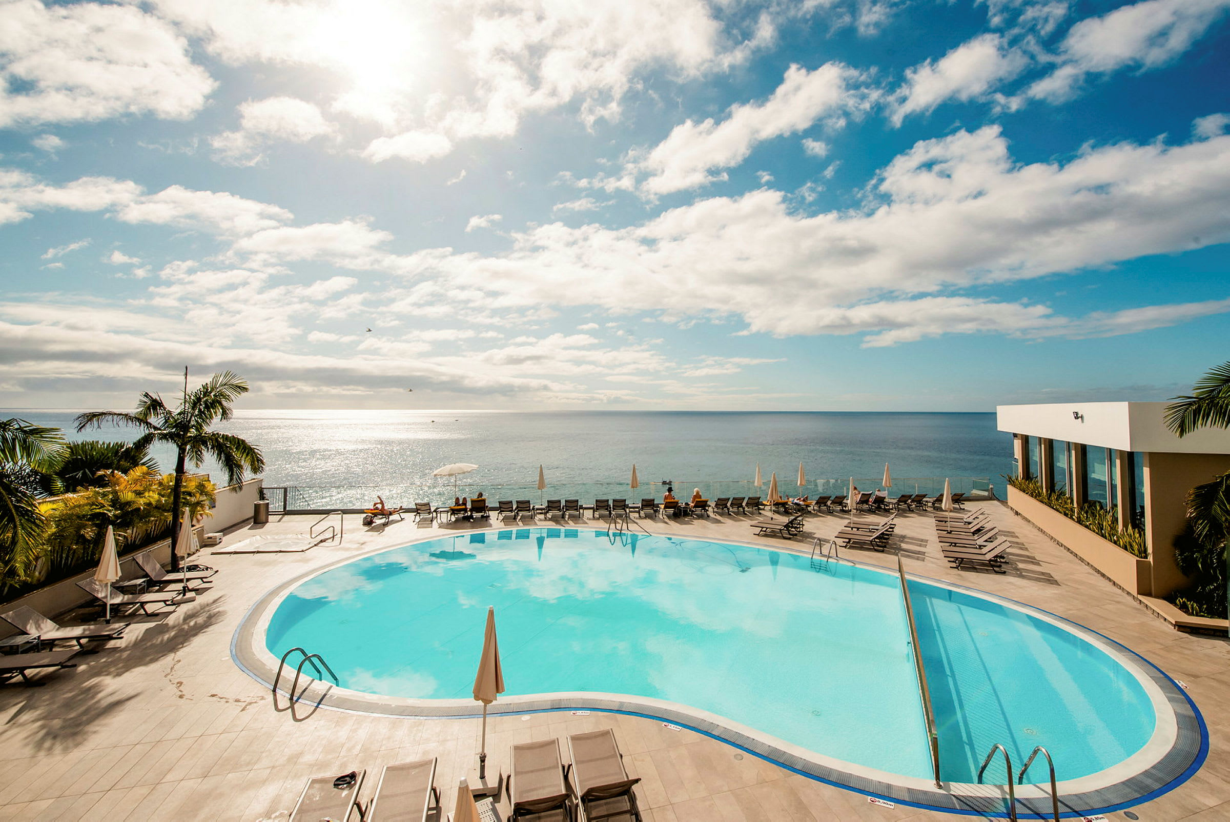 Poolområde med udsigt over havet under en klar himmel. (AI-genereret tekst)